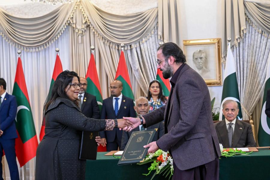 A Maldivian official in a black dress exchanges a folder with a Pakistani official while Prime Minister Sharif watches from the table.
