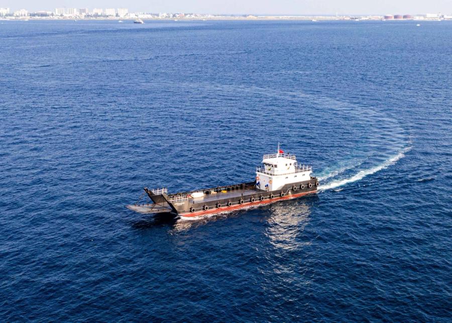 A landing craft with a bow ramp turning on open sea, a city skyline on the horizon