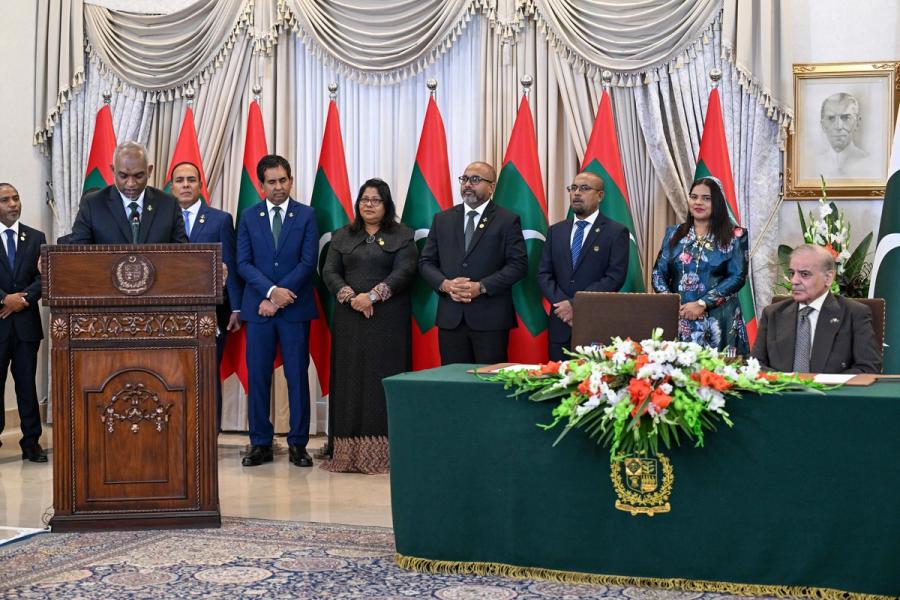 A wide view of President Muizzu at the lectern while Prime Minister Sharif sits at the signing table and the Maldivian delegation stands behind.