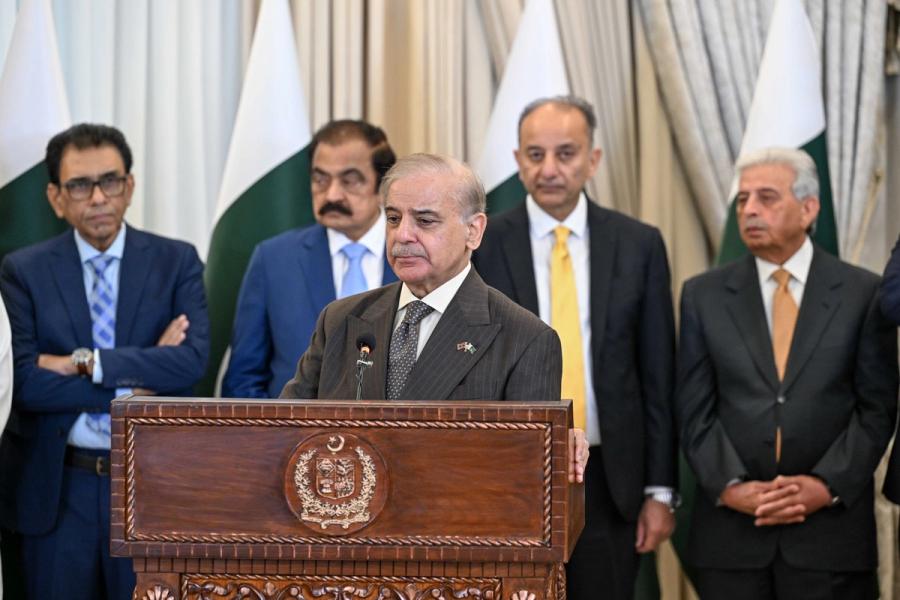 Prime Minister Shehbaz Sharif speaks at a carved wooden lectern, with Pakistani officials standing behind him.