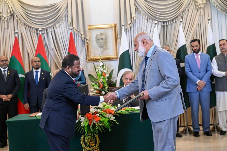 A Maldivian official and a Pakistani official in a grey suit shake hands as they exchange folders.