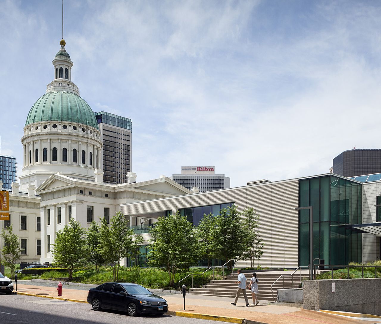 People walking in front of the New plaza at the corner of chestnut and north broadway in downtown st louis with the city capitol building in the background.