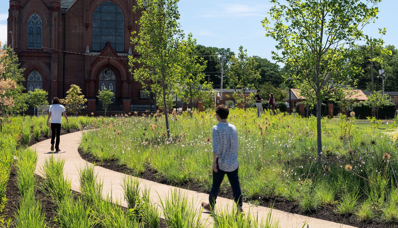 People walking on path in Carillon Park with native plantings and view of a church. Designed by arbolope studio.