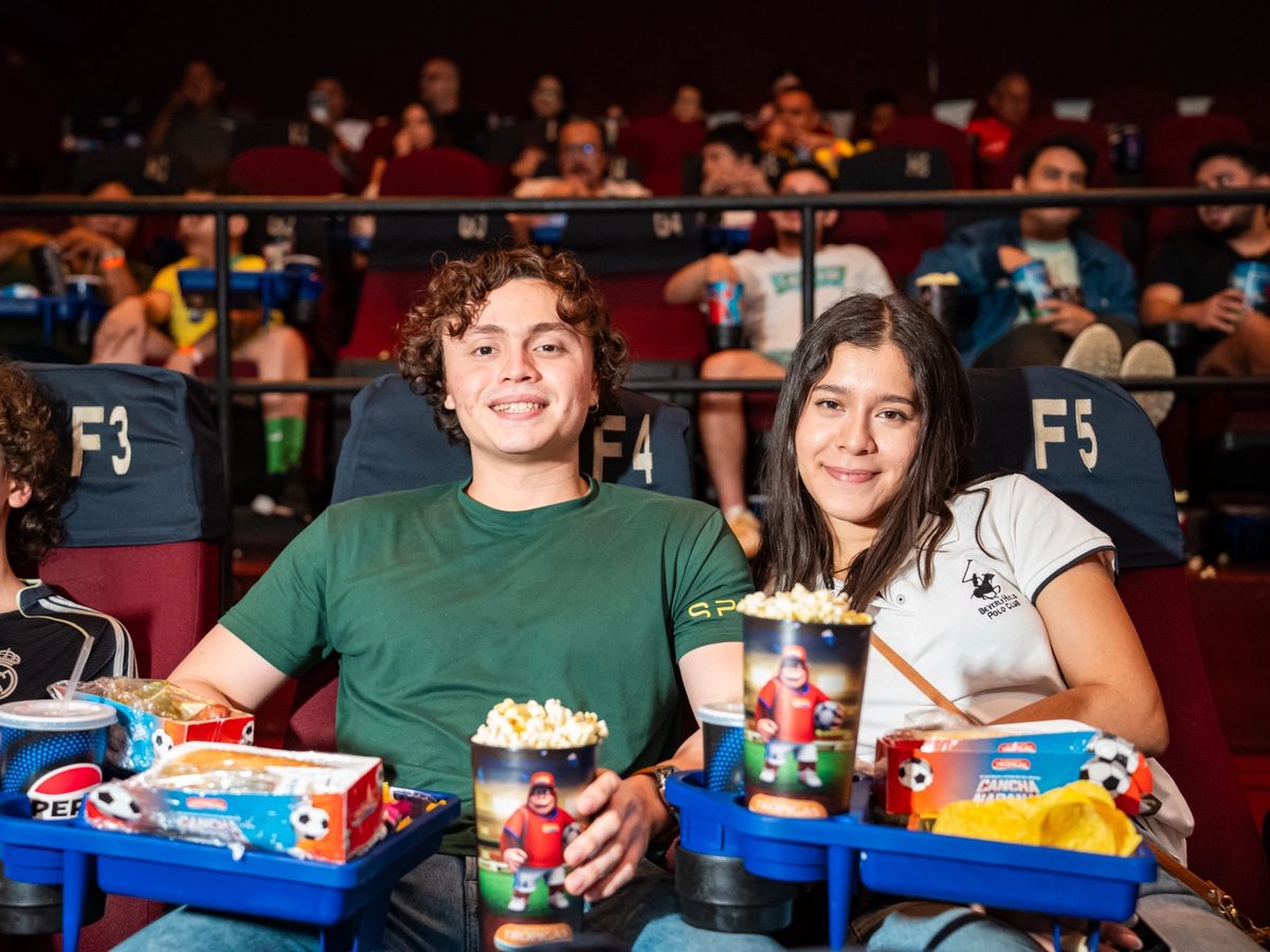 Dos jóvenes en sus butacas con bandejas de combos y vasos de la promoción.