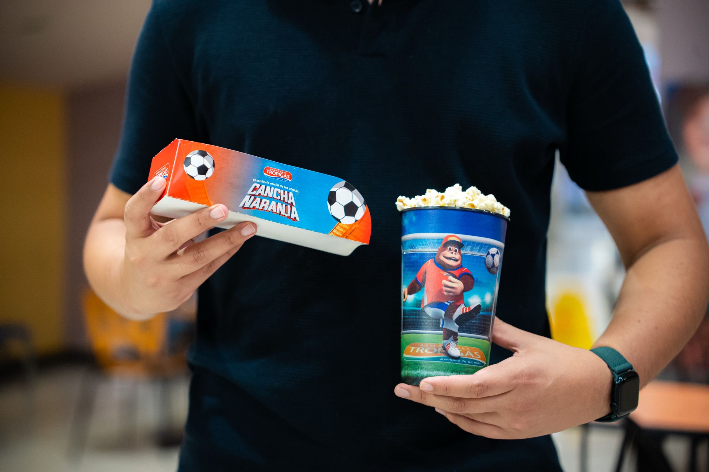 Manos sosteniendo la caja de combo y el vaso de Cancha Naranja.