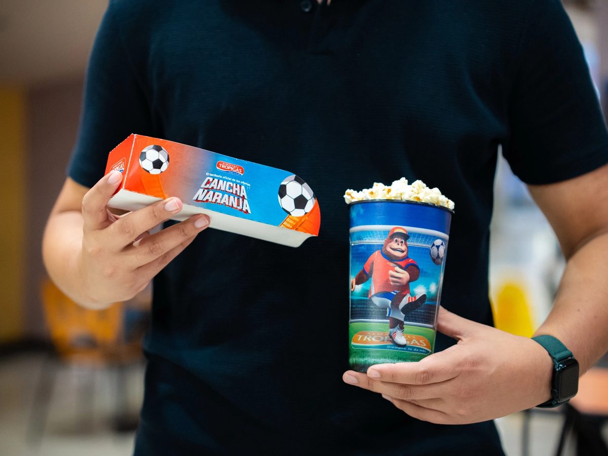 Manos sosteniendo la caja de combo y el vaso de Cancha Naranja.