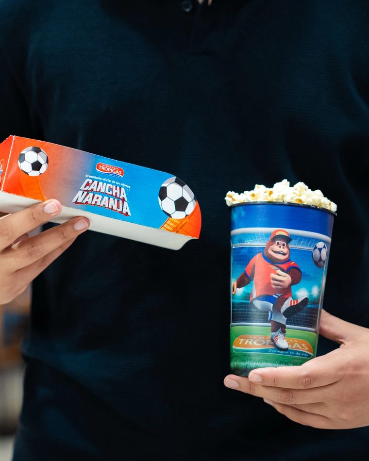 Manos sosteniendo la caja de combo y el vaso de Cancha Naranja.