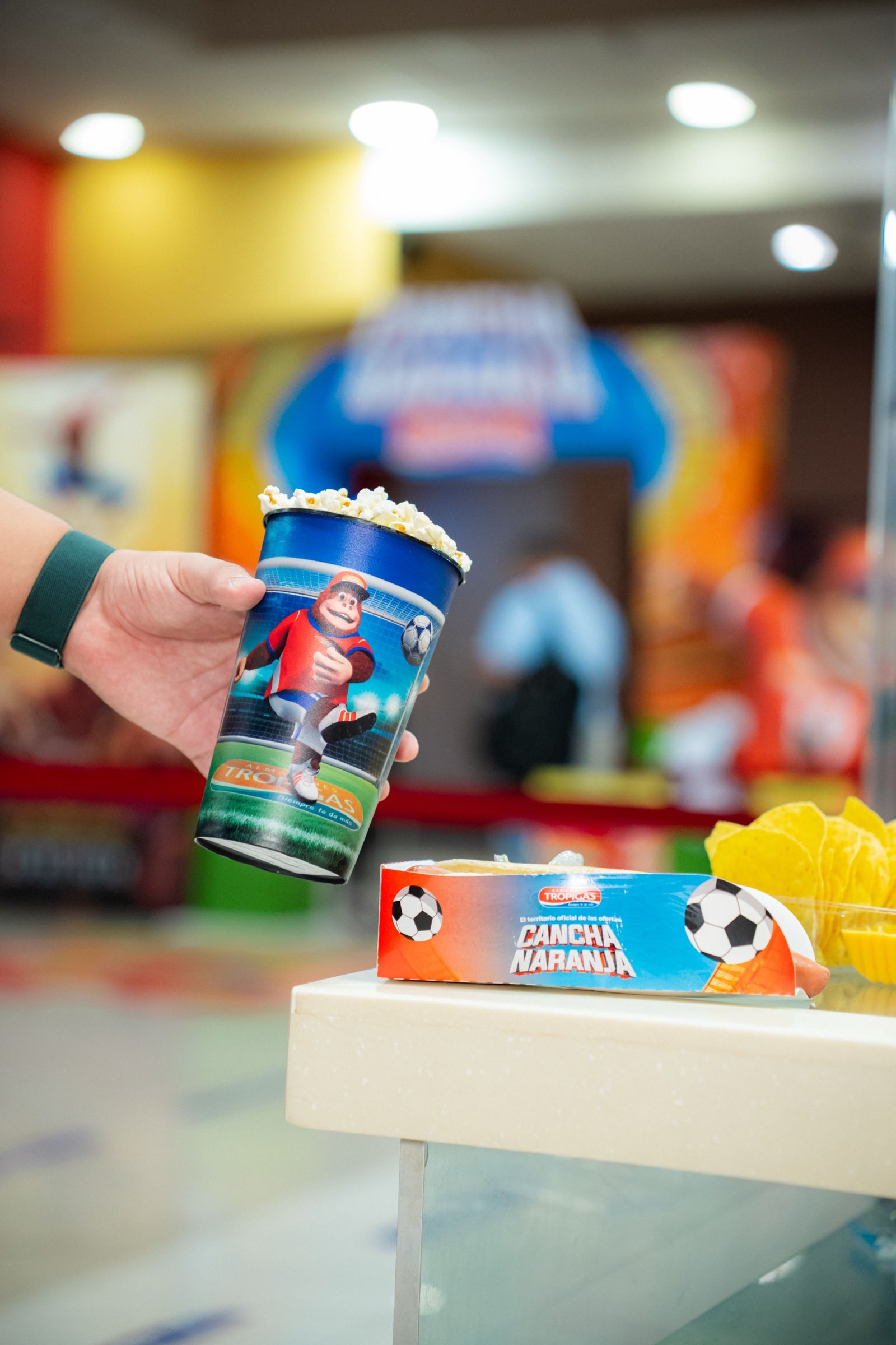 Vaso y caja de combo de Cancha Naranja sobre el mostrador de la dulcería.