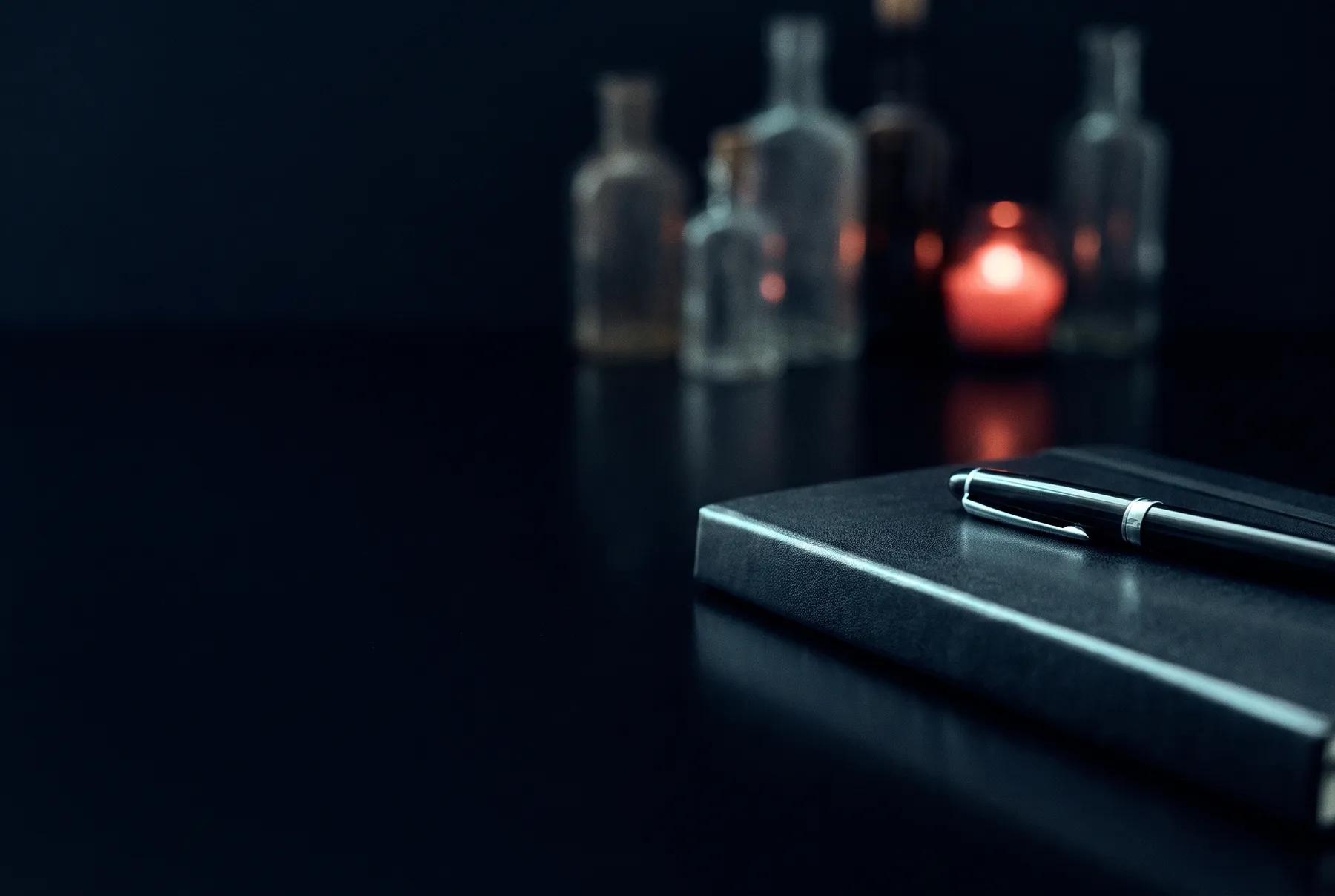 Cuaderno cerrado con una pluma encima sobre una mesa oscura y reflectante, con frascos desenfocados y una luz roja al fondo