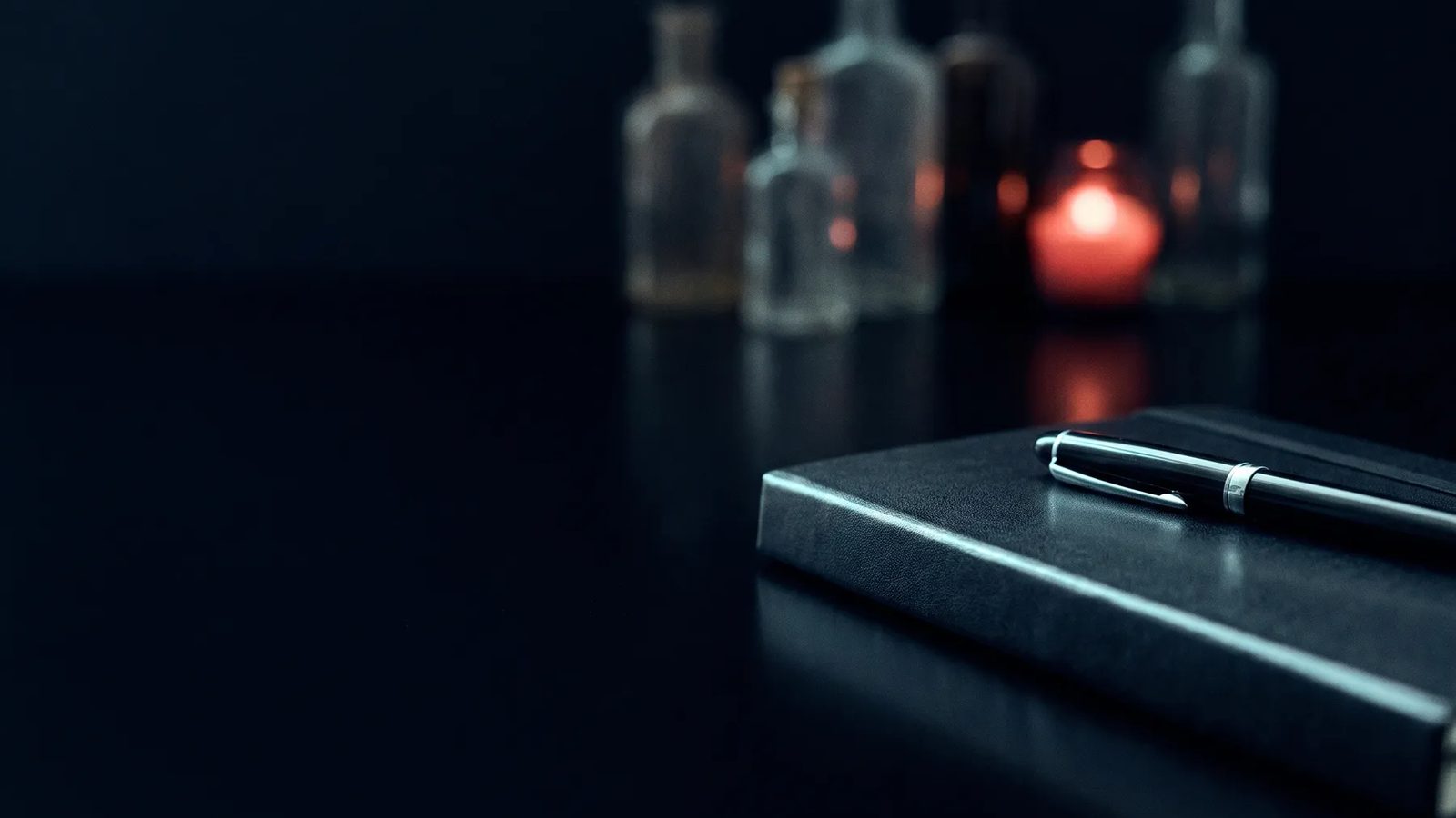 Cuaderno cerrado con una pluma encima sobre una mesa oscura y reflectante, con frascos desenfocados y una luz roja al fondo