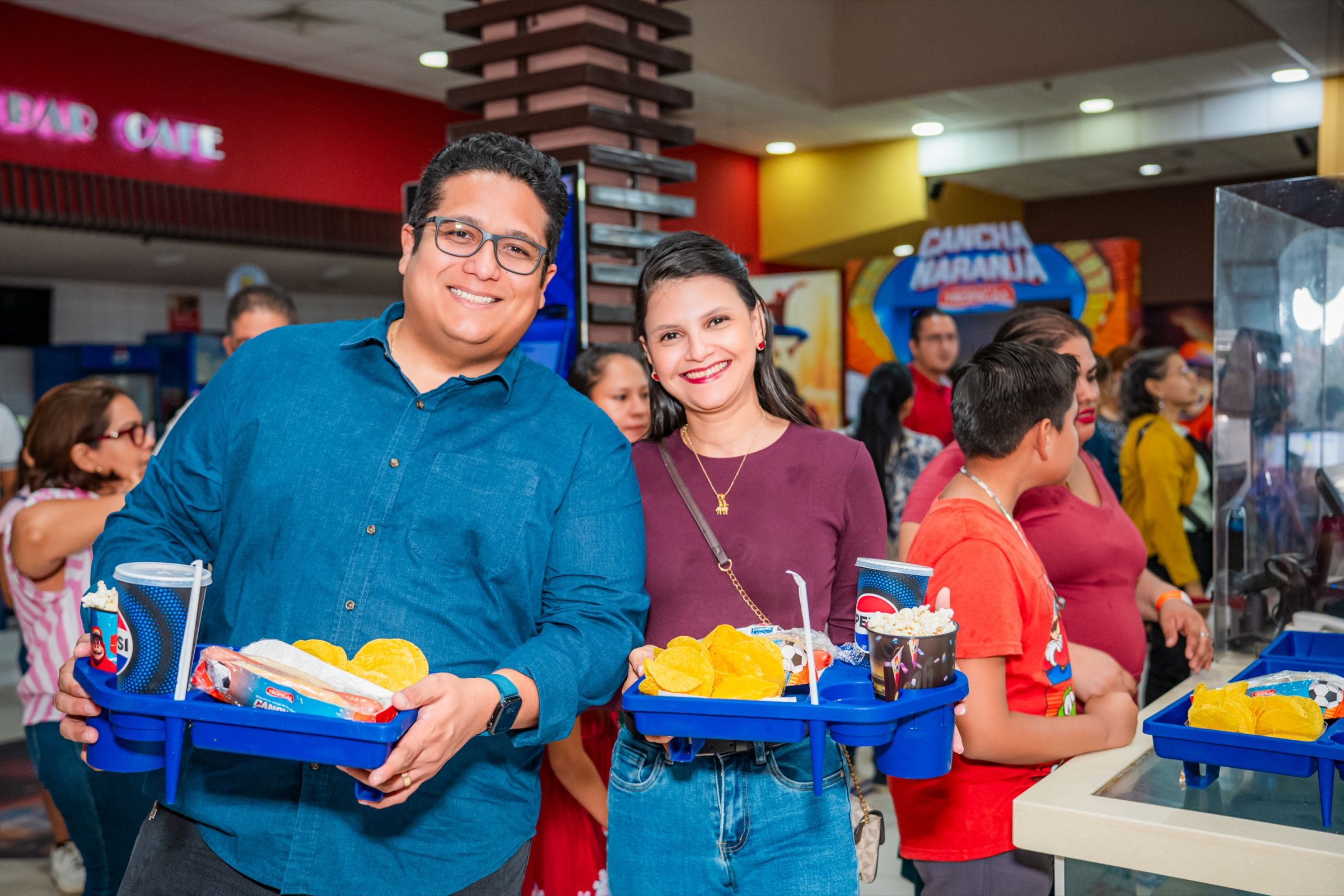 Dos clientes en la dulcería del cine con bandejas de combos de Cancha Naranja.