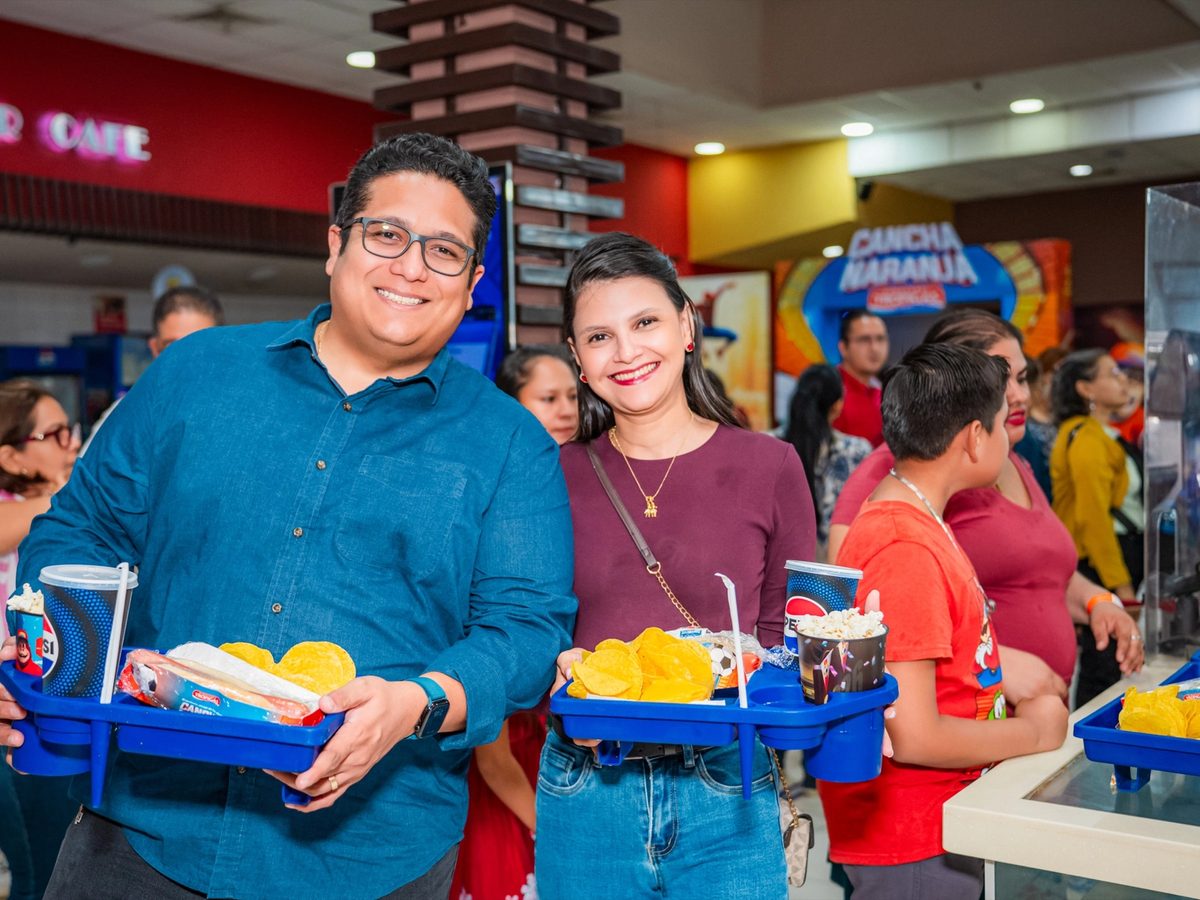 Dos clientes en la dulcería del cine con bandejas de combos de Cancha Naranja.