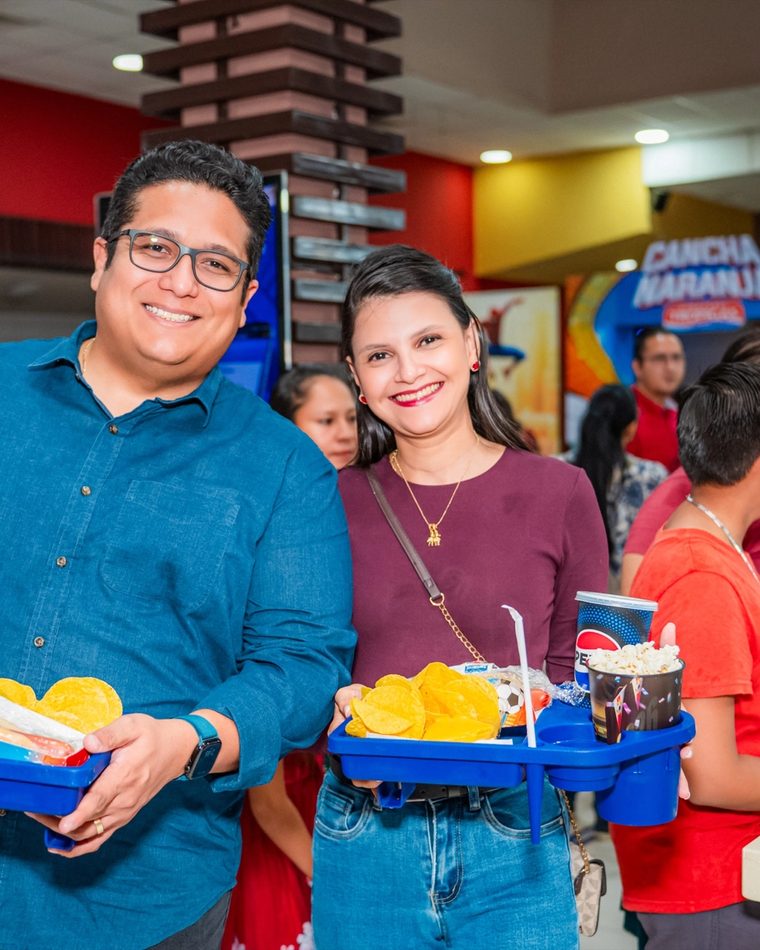 Dos clientes en la dulcería del cine con bandejas de combos de Cancha Naranja.