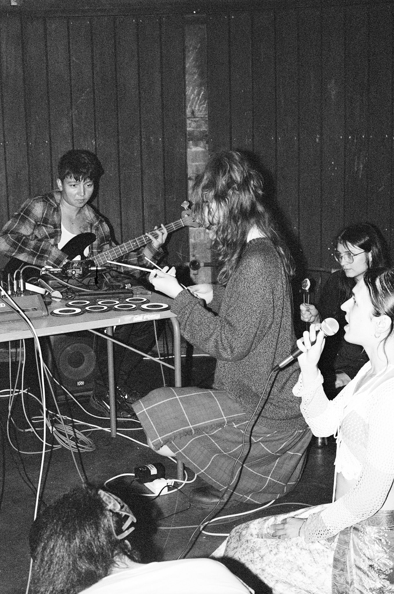 multiple people sat on the floor, one playing a guitar, another singing into a mic, another with drum sticks