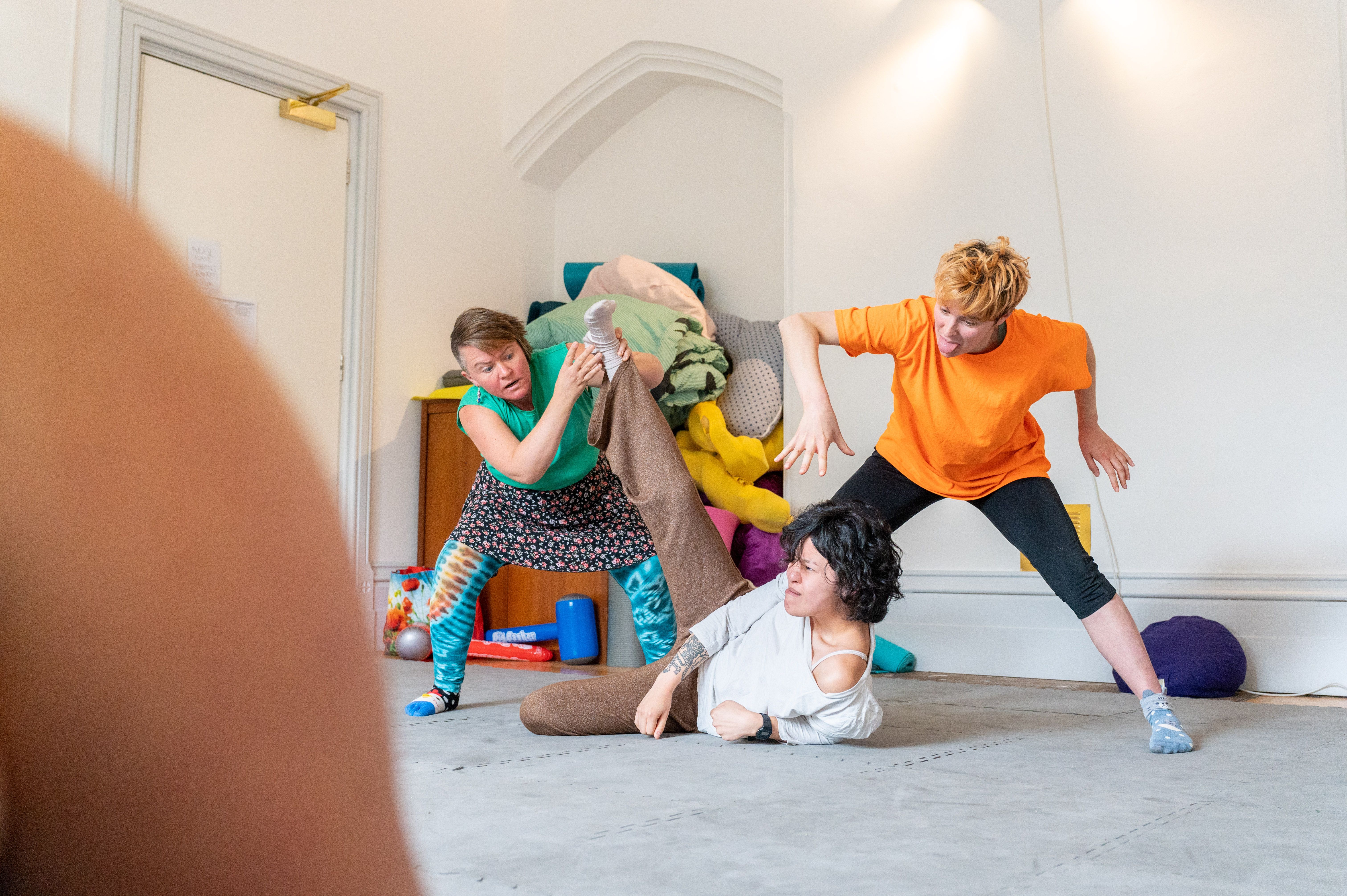 3 people in bright coloured outfits, clowning around in the movement room, with big body language and expressive faces