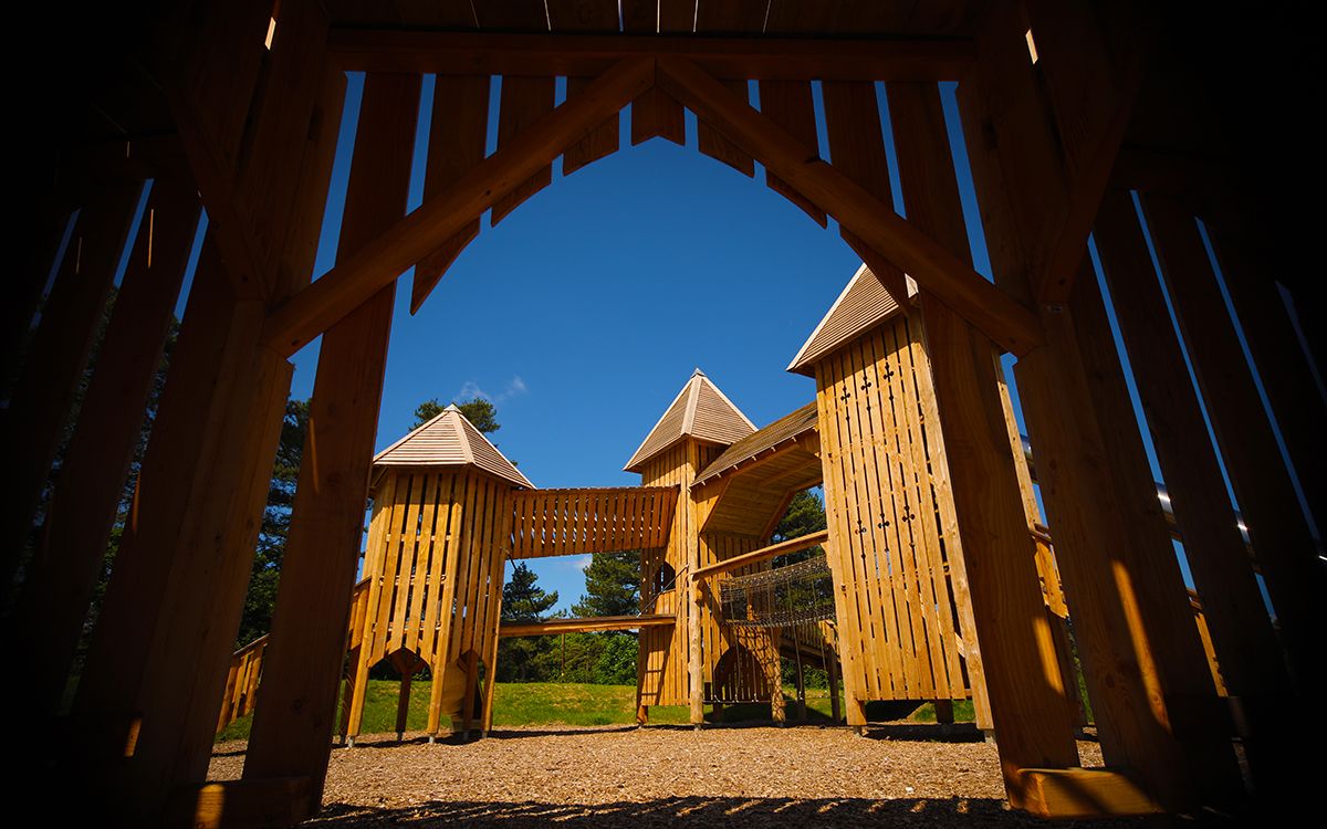 Photograph of wooden play facilities at Wyvernwood visitor attraction. The photo is taken from inside a wooden play building and is looking towards a children's outdoor climbing and play structure. Photo credit: www.wyvernwood.co.uk