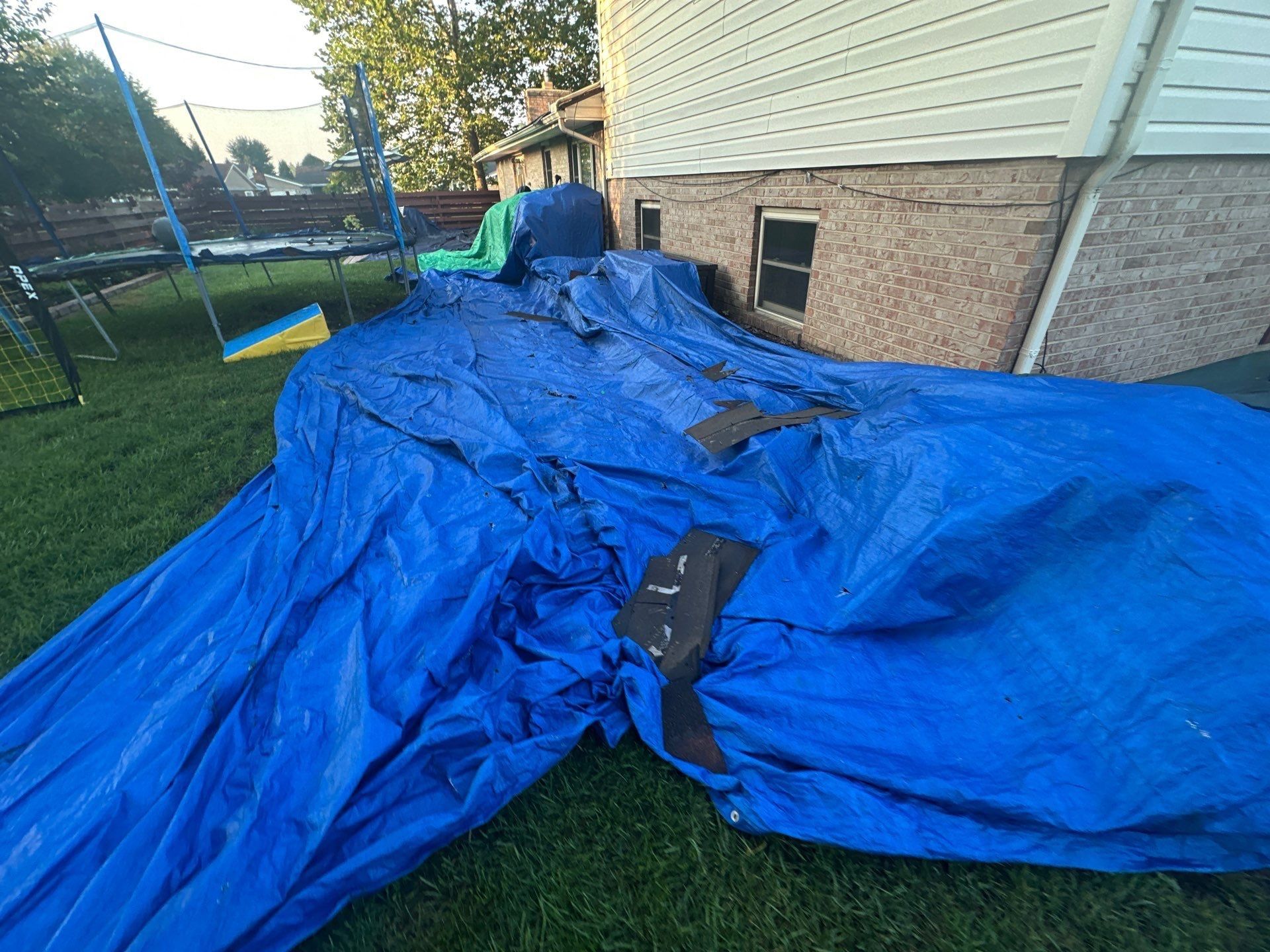 Blue tarps over the back flower beds, with the trampoline and fence beside them, Dayton, Ohio.