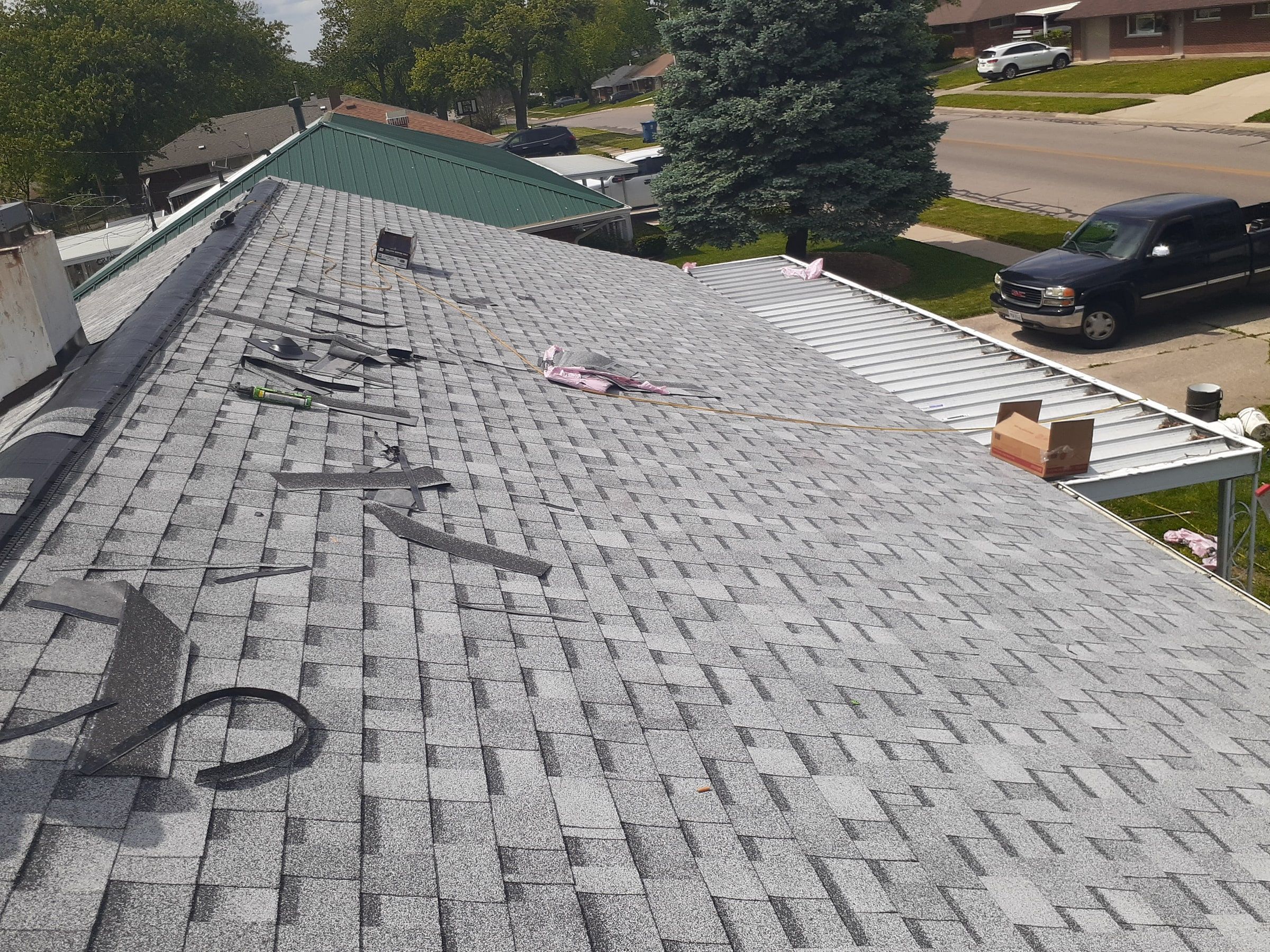 A long run of new shingles toward the street, with tools on the roof, Huber Heights, Ohio.