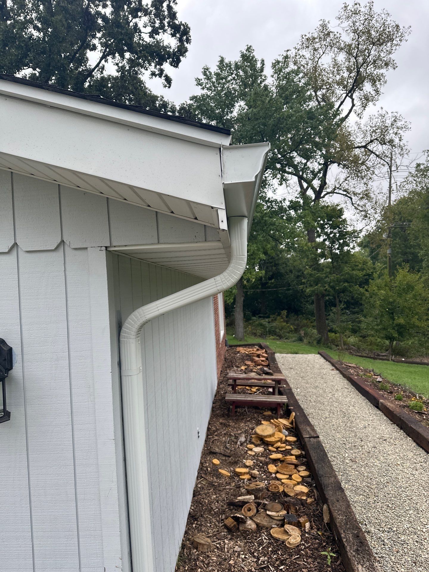 The new downspout elbow and run down the garage siding, with the gravel path beyond.