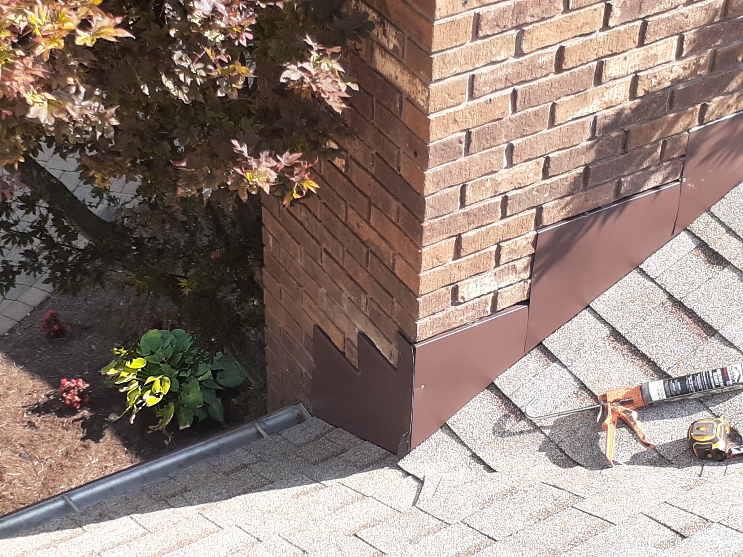 Chimney corner wrapped in new metal flashing with sealant at hand, Jamestown, Ohio.