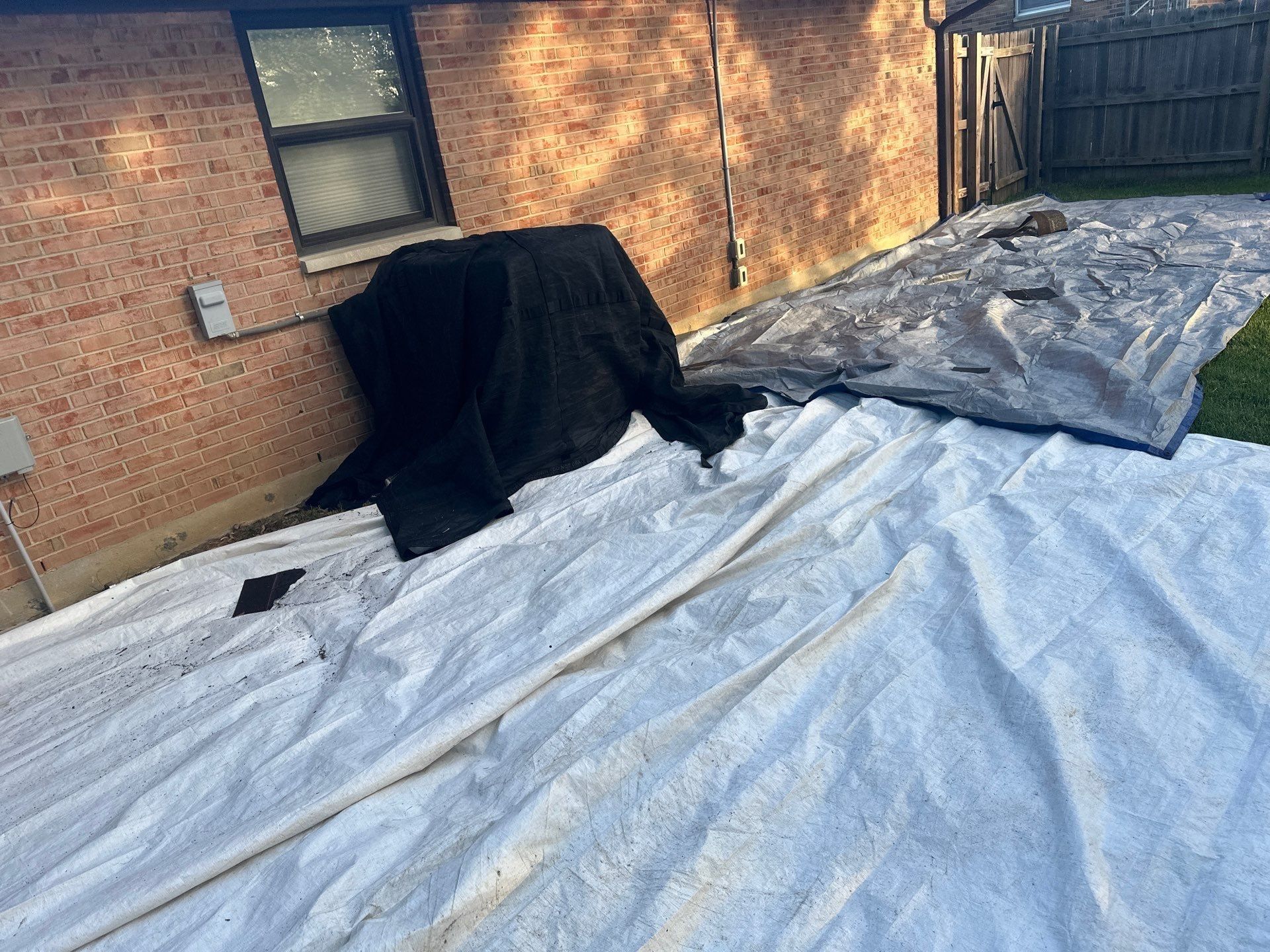 A dark tarp covering a shrub beside the back wall, Beavercreek, Ohio.