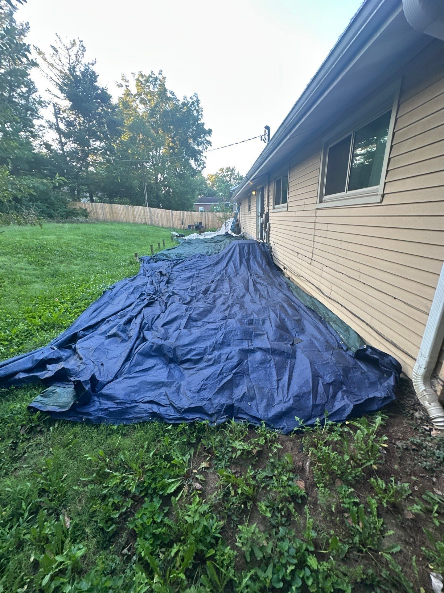 A blue tarp laid along the back wall of the house over the lawn, Fairborn, Ohio.