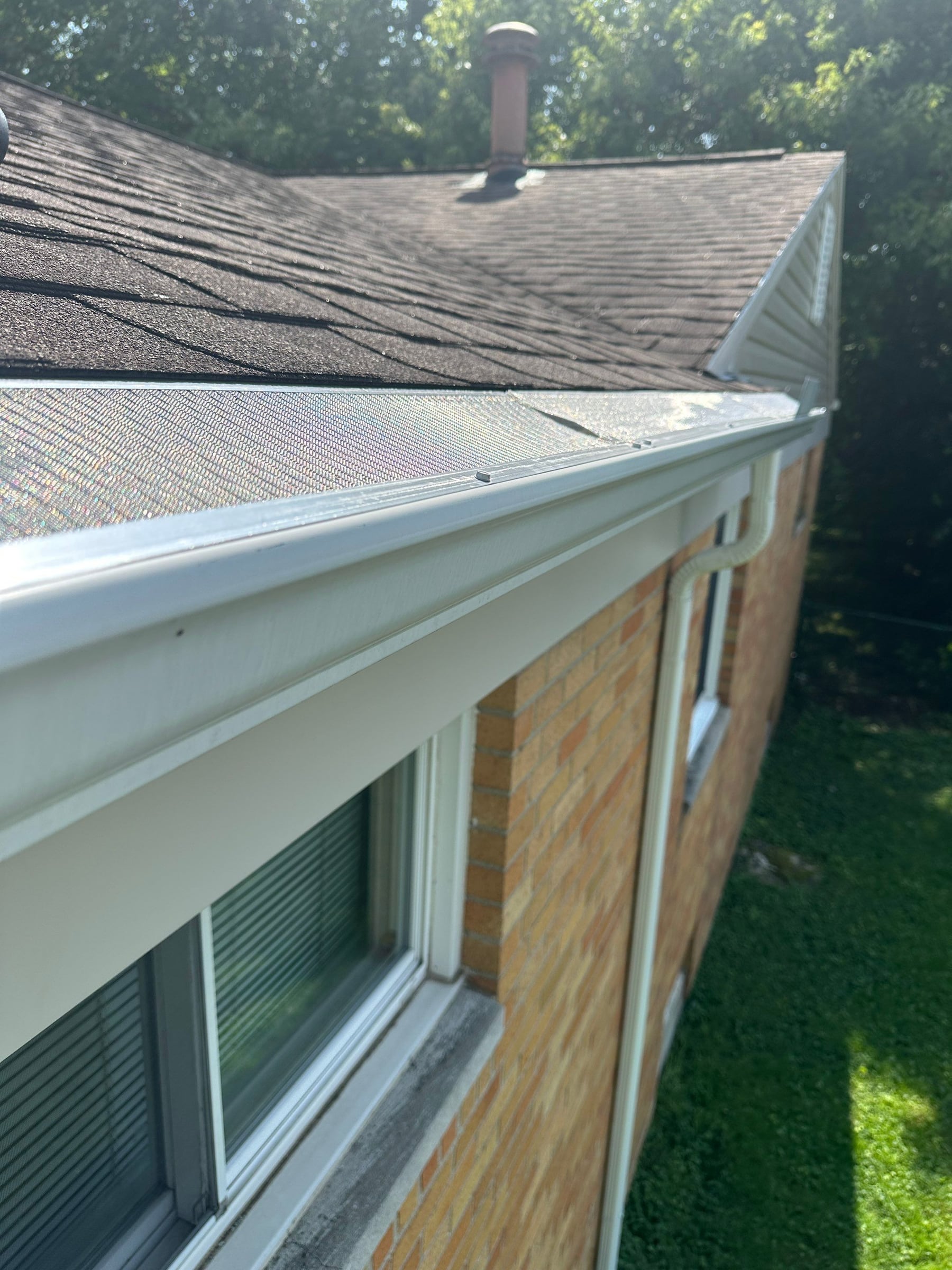 A finished gutter guard running the length of the eave on a brick ranch, the gutter and downspout below it.