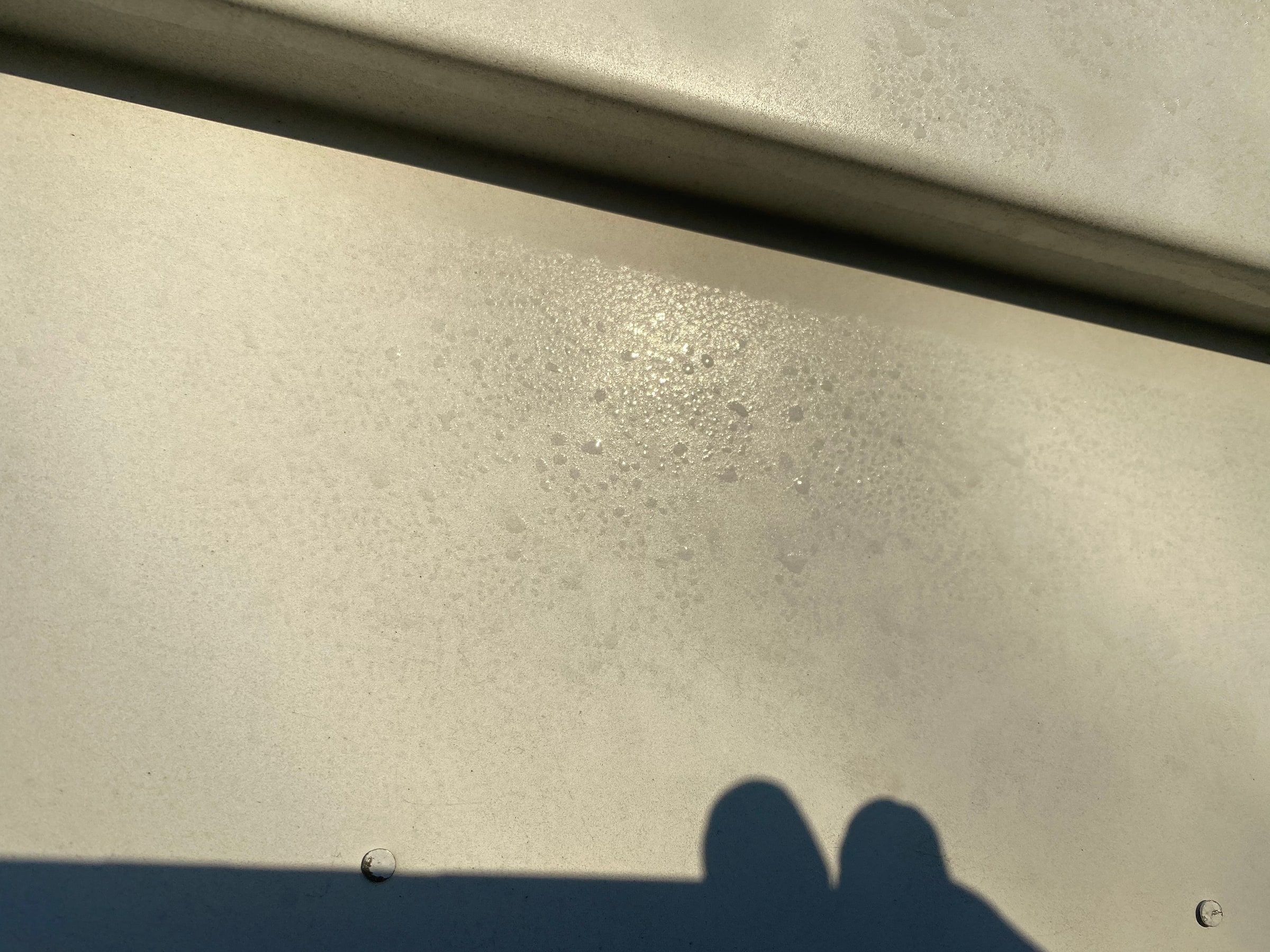 A dented section of gutter still on the fascia, dimpling visible across its face in raking light.