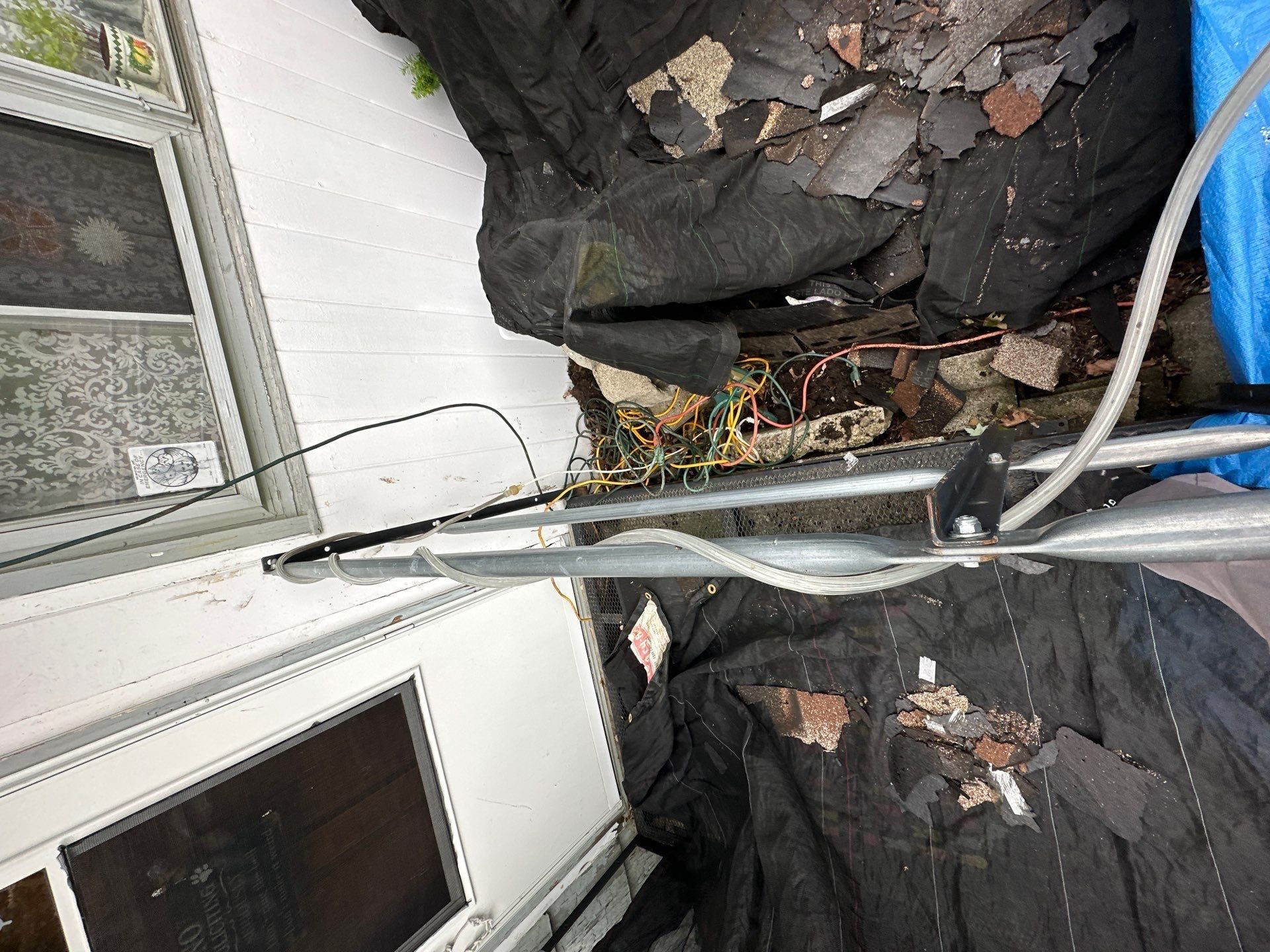 Black tarps, shingle pieces and extension ladder