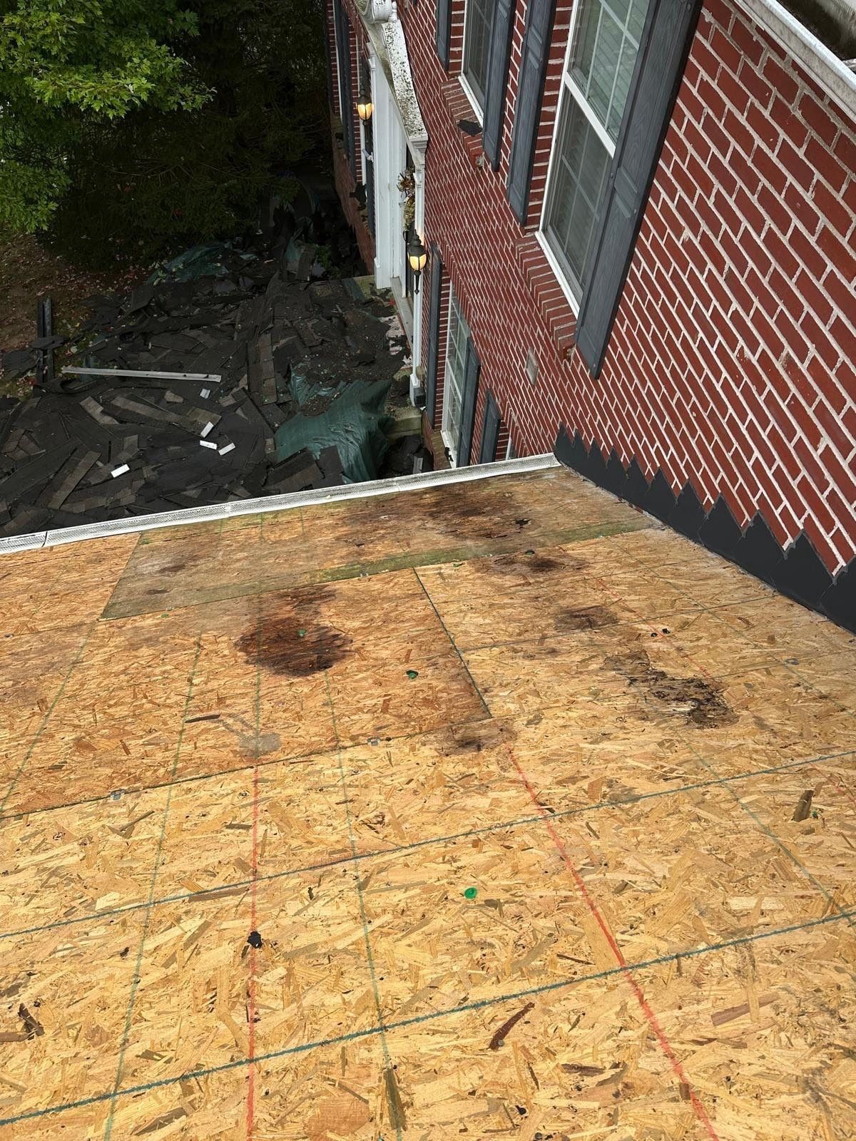Water stains on the bare deck of the lower roof beside the brick wall, Beavercreek, Ohio.