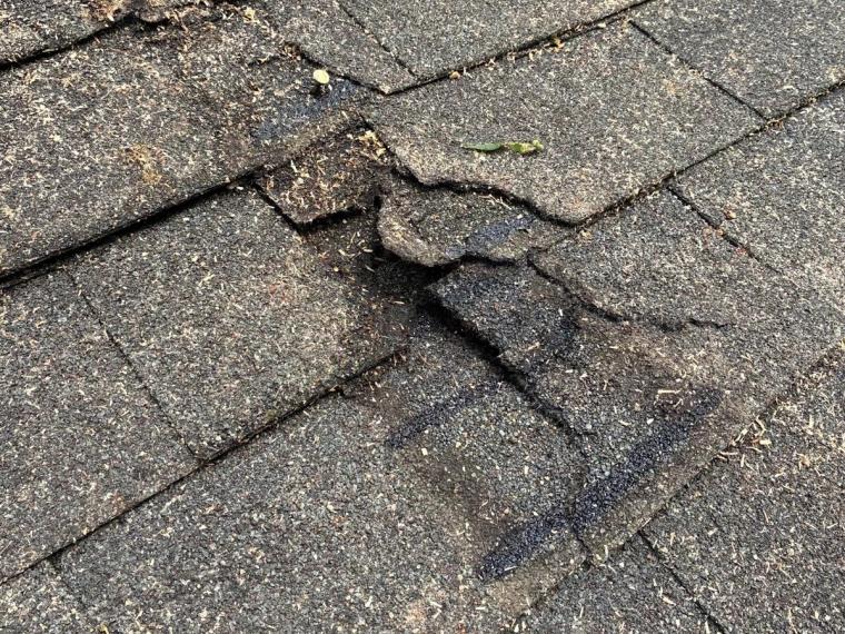 A split torn through the shingle courses, the layers beneath showing through.