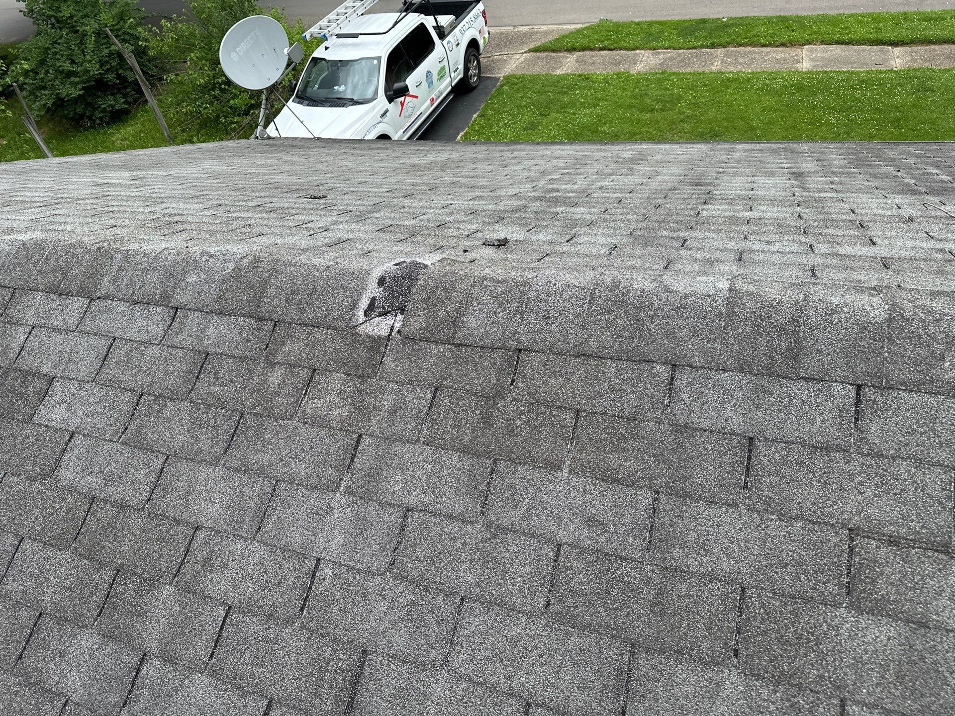 A wind-damaged shingle missing from the ridge, with the work truck below, Dayton, Ohio.