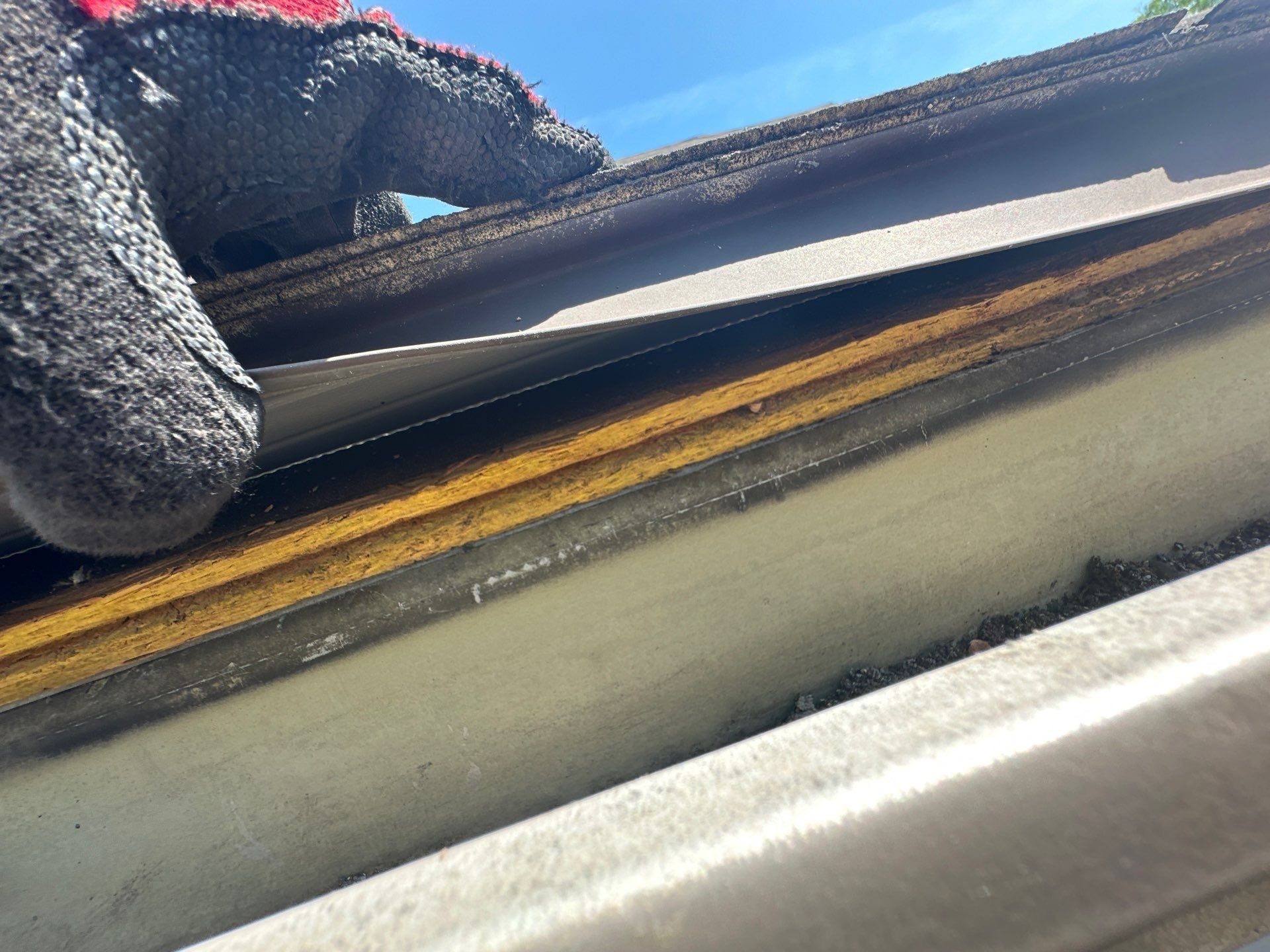 A gloved hand lifting the shingle edge to show the plywood decking, Kettering, Ohio.