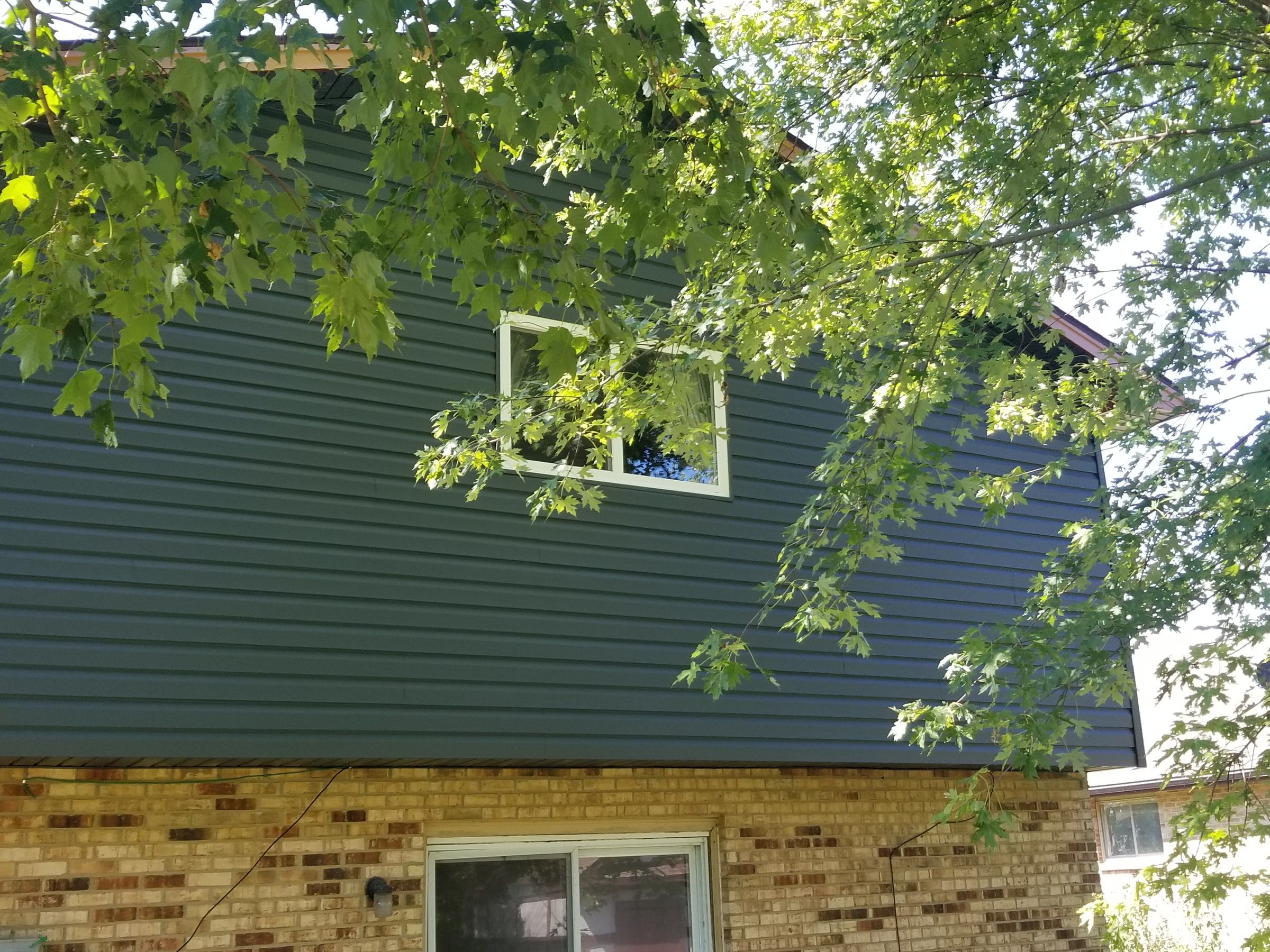 The upper back wall in blue-gray siding through the tree branches, Beavercreek, Ohio.