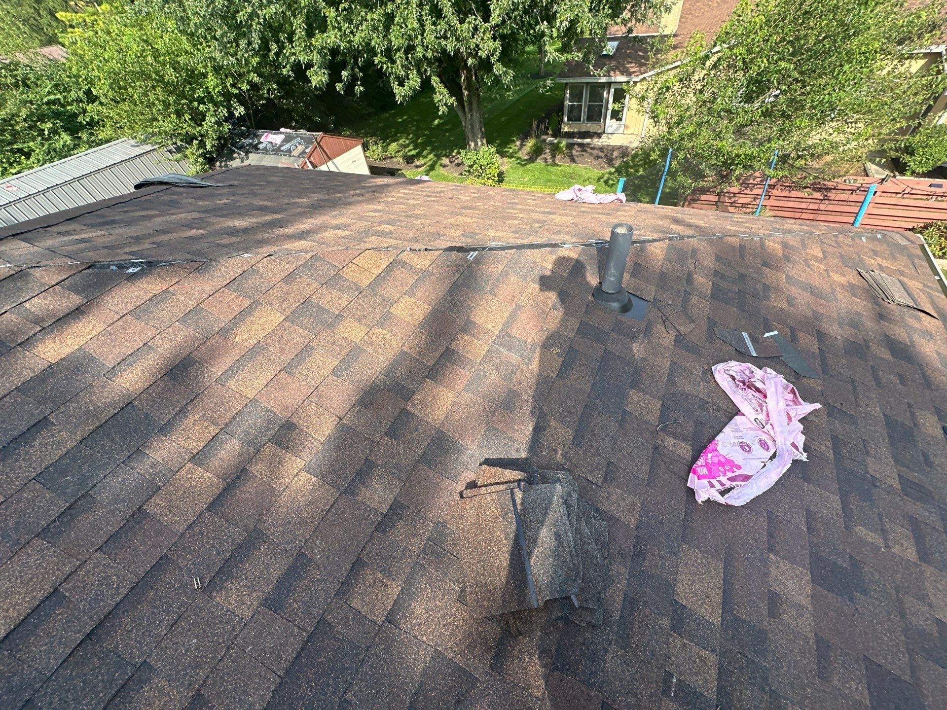 New shingles on the back slope around a vent pipe, with wrapper scraps on top, Dayton, Ohio.
