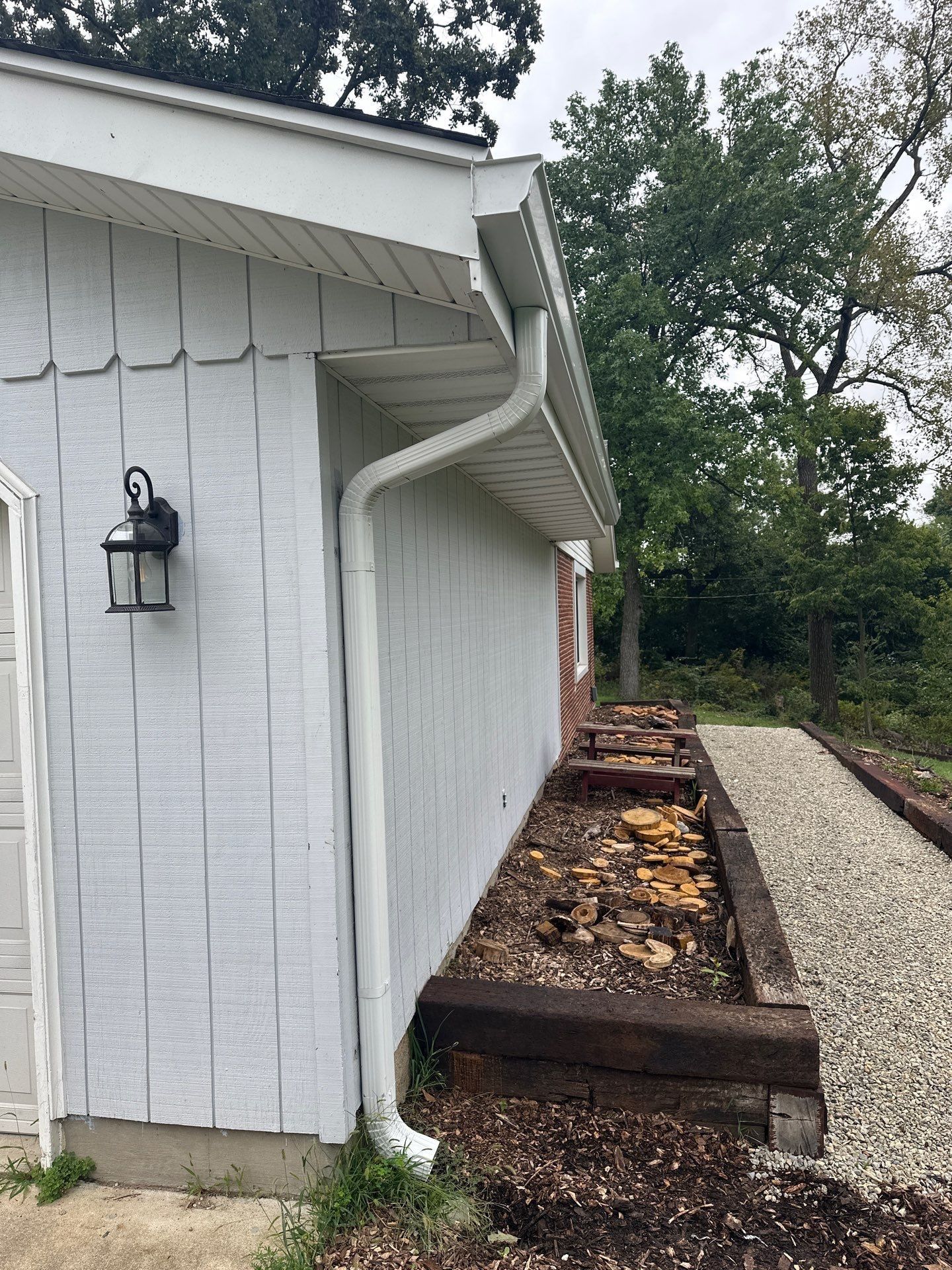 A new downspout at the corner of the white-sided wall above a gravel path, West Carrollton, Ohio.