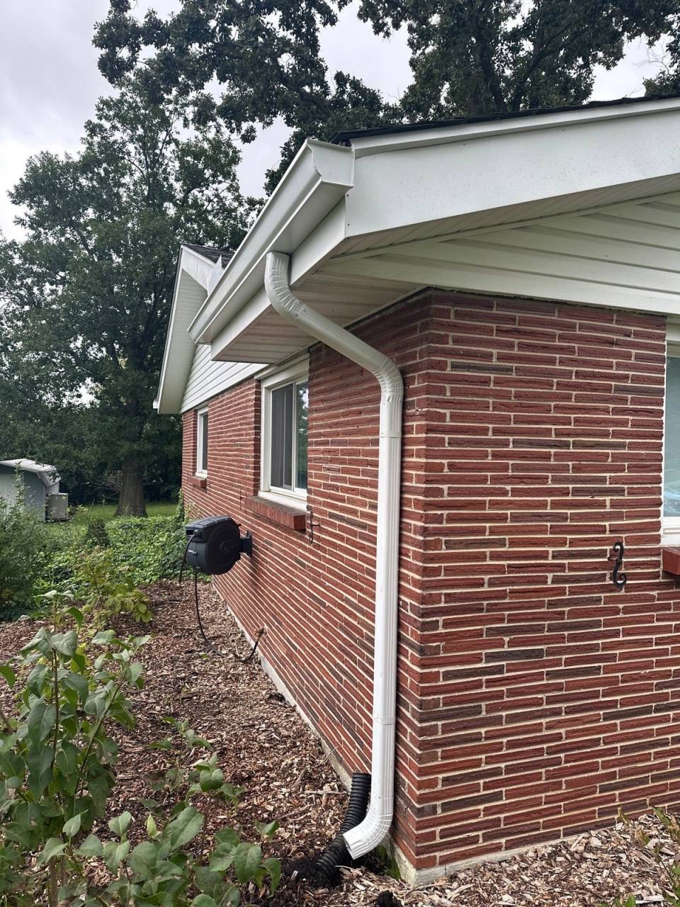A new white downspout carried down the brick corner from the new gutter above.