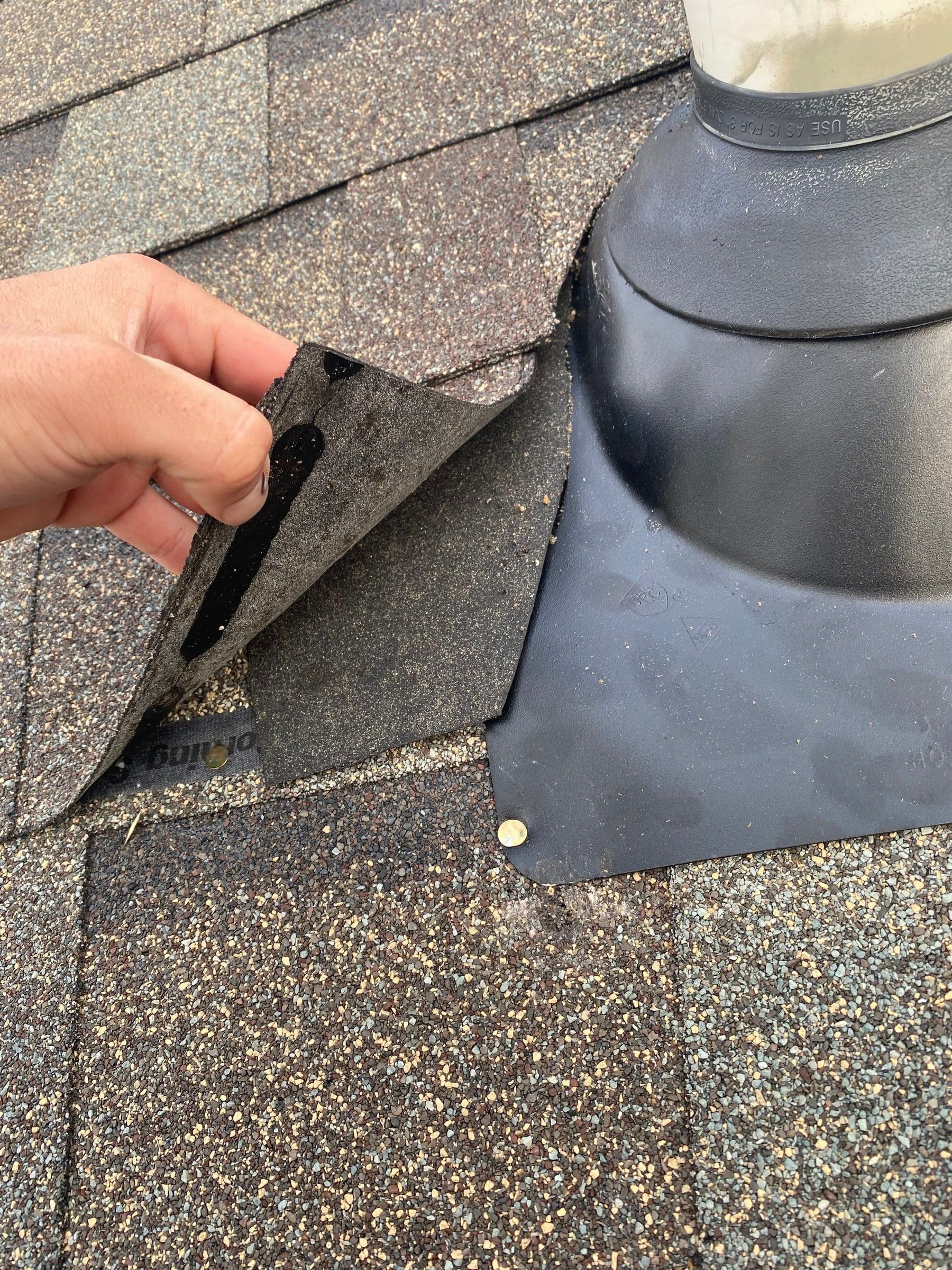 Hand lifting an unsealed shingle beside a plumbing vent boot, Yellow Springs, Ohio.