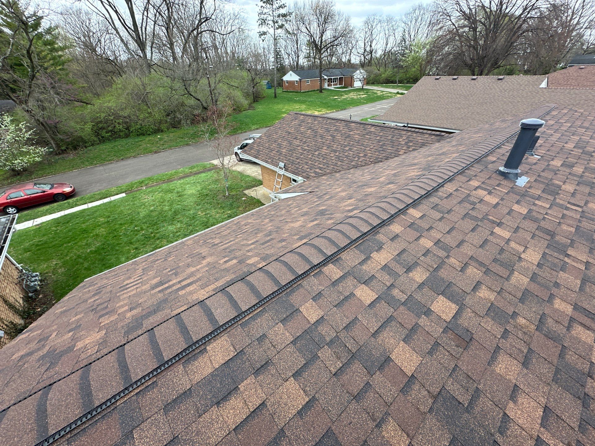 A rebuilt roof on a Dayton, Ohio home, its capped ridge running away past the vent toward the street.