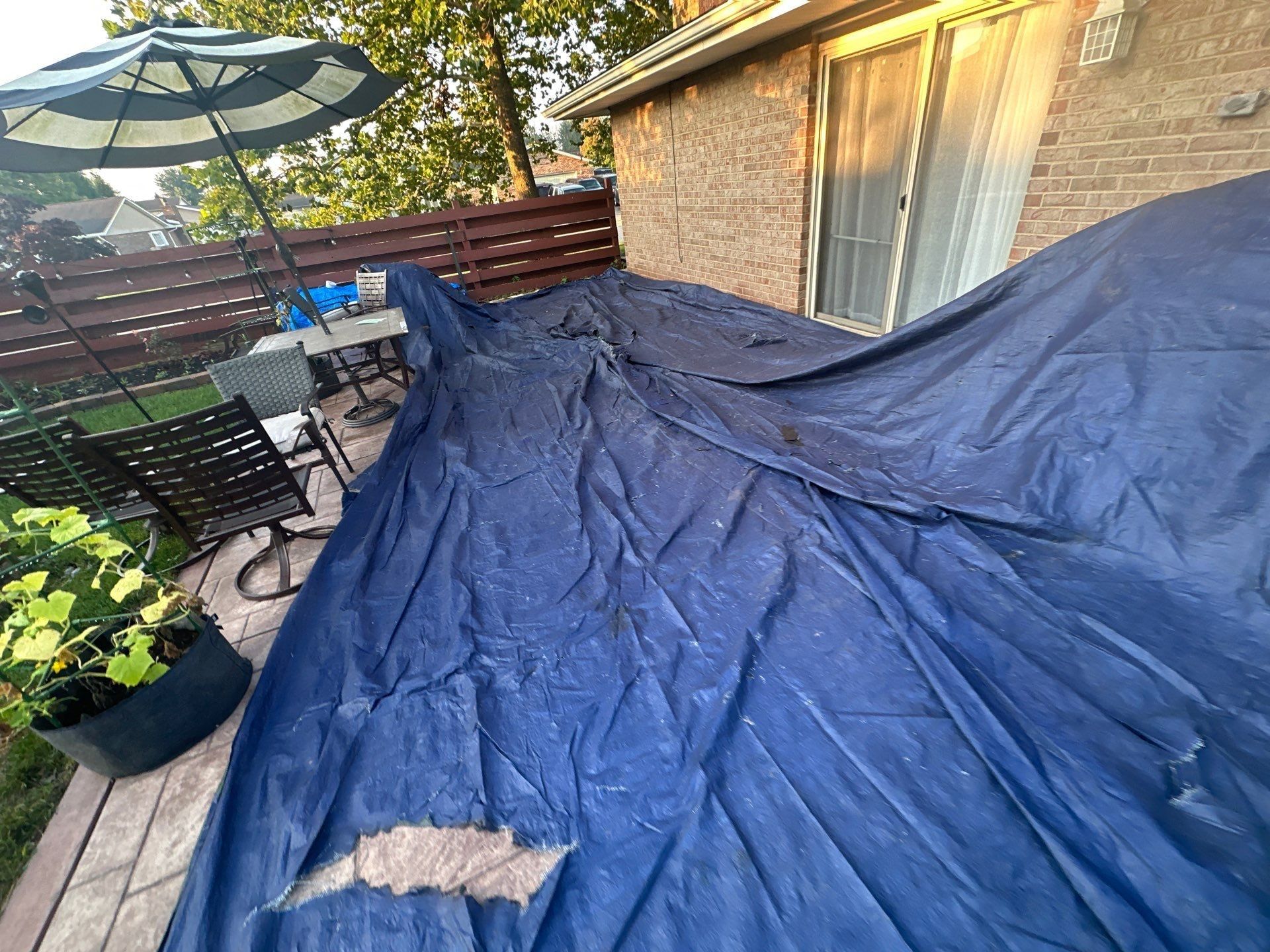 A navy tarp across the deck, with patio chairs and an umbrella beside it, Dayton, Ohio.