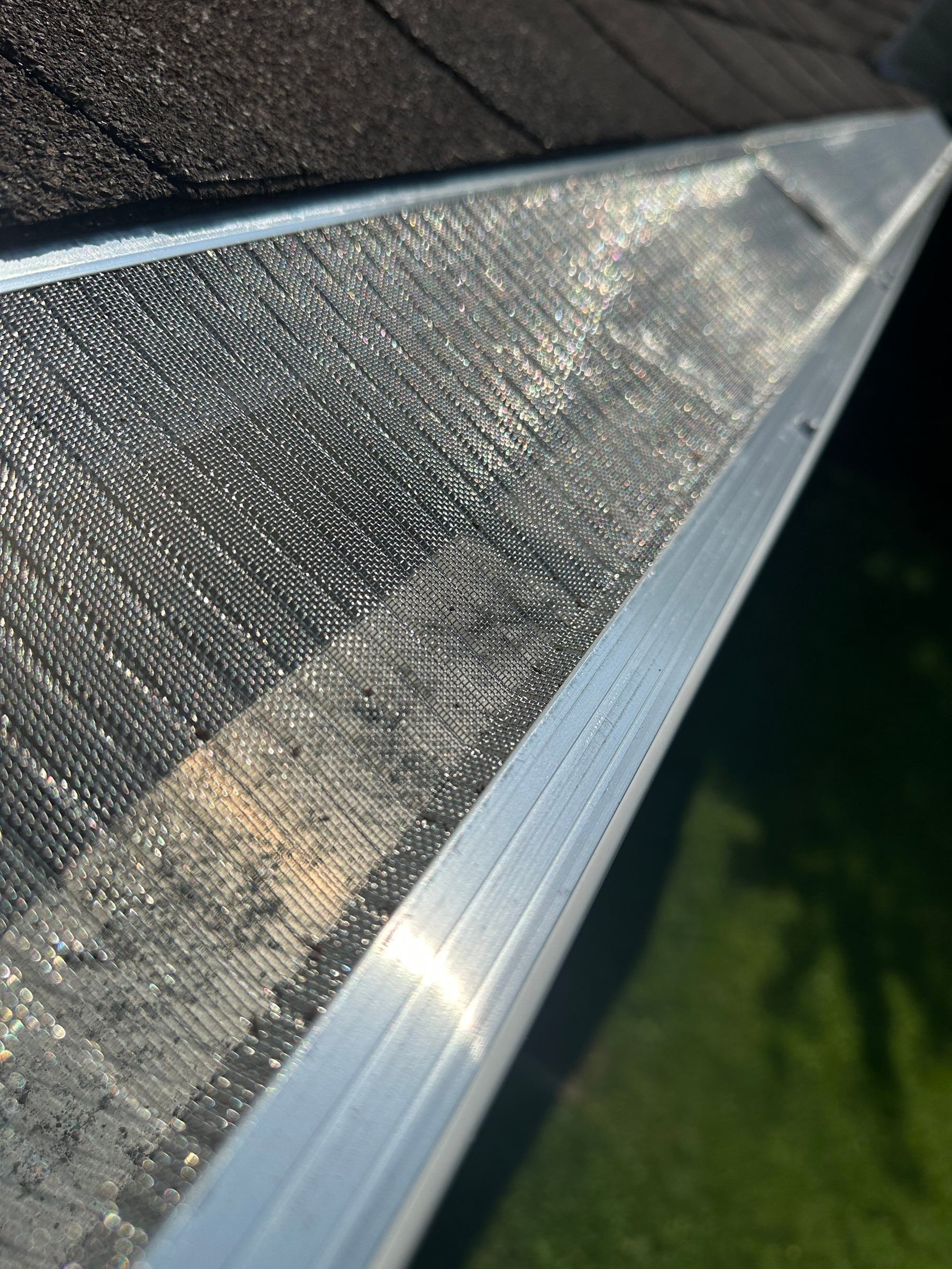The stainless mesh of a gutter guard close up, its weave filling the frame beside the outer lip of the gutter.