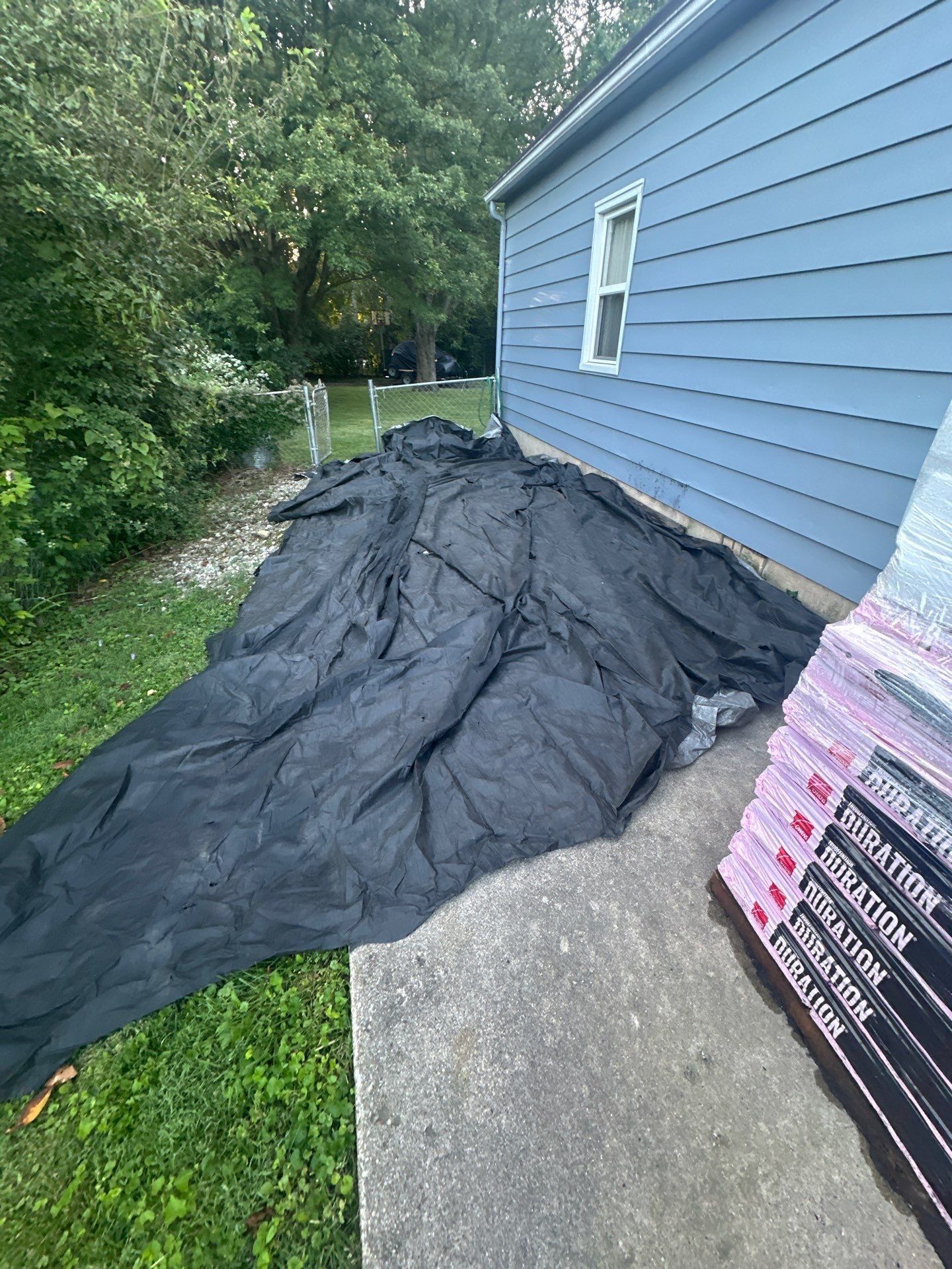 A tarp spread along the side of the house beside the shingle pallets, Beavercreek, Ohio.