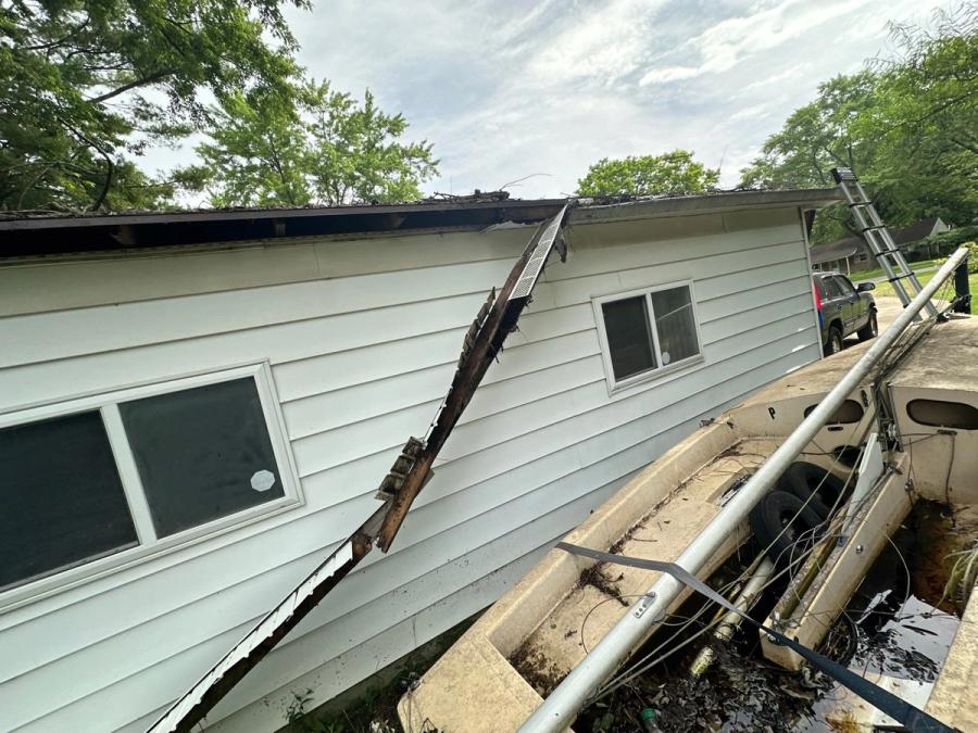 The outbuilding eave with the fascia torn away and hanging down the wall, and the soffit missing behind it.