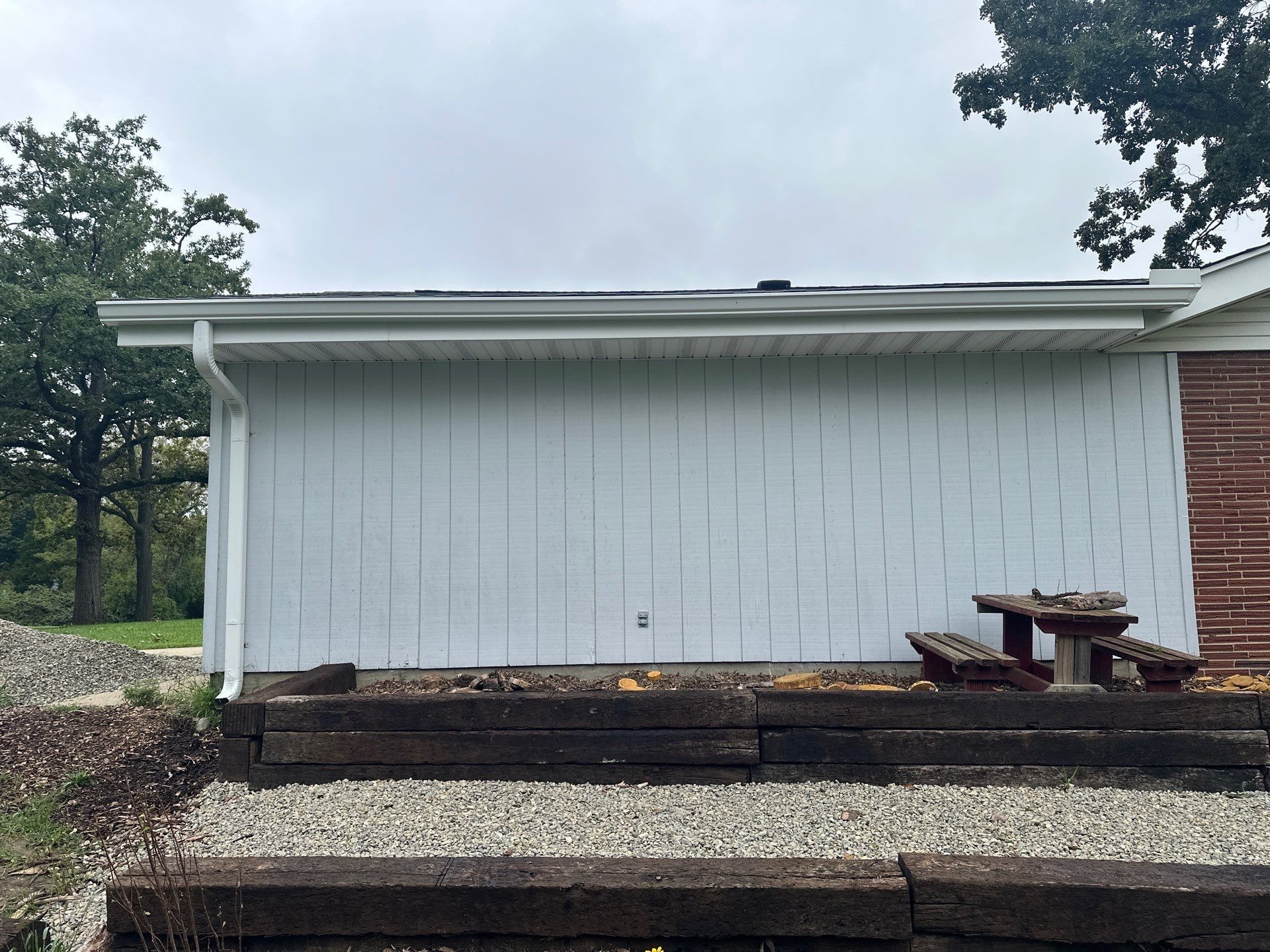 The white-sided garage wall with a new seamless gutter along its eave and a downspout at the end.