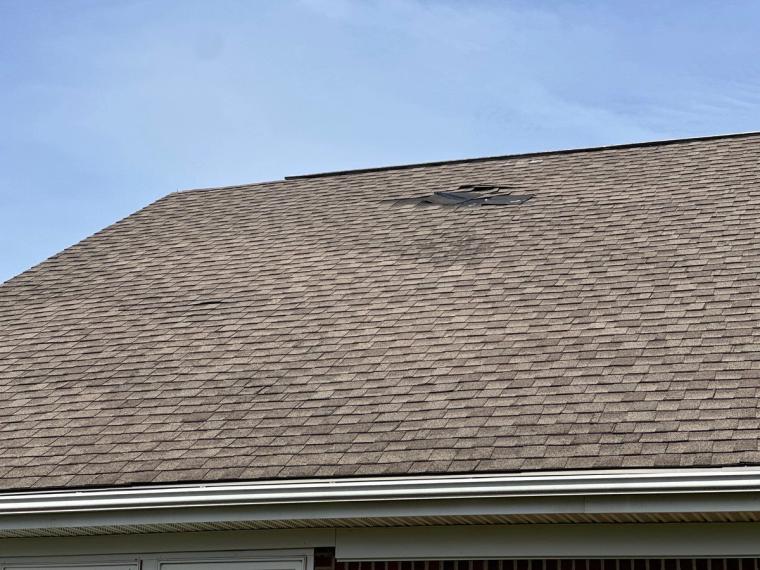 Shingles torn away from the roof slope below the ridge, exposing the layer underneath.