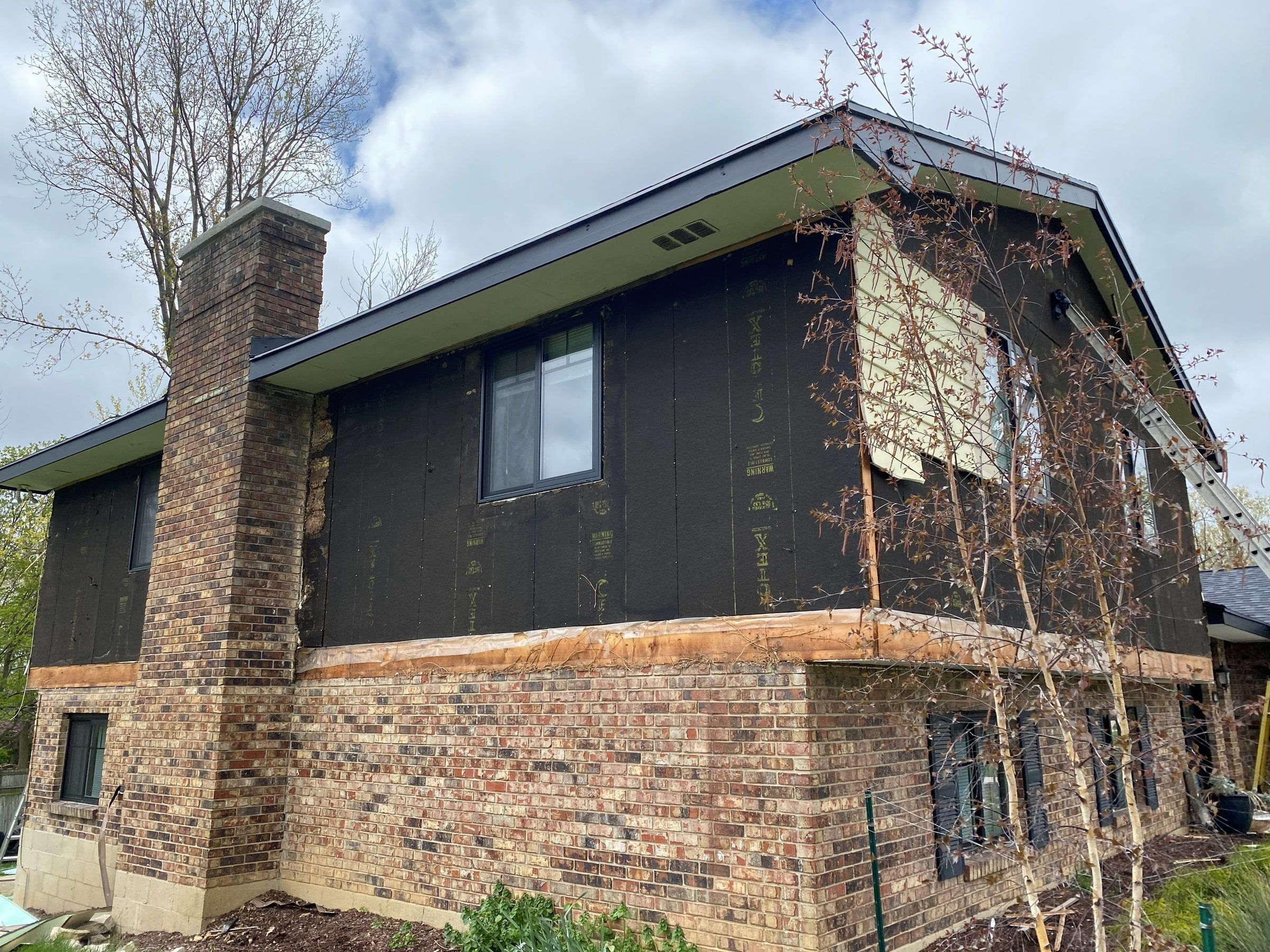 The chimney side of the house with builder board exposed on the upper story, Beavercreek, Ohio.