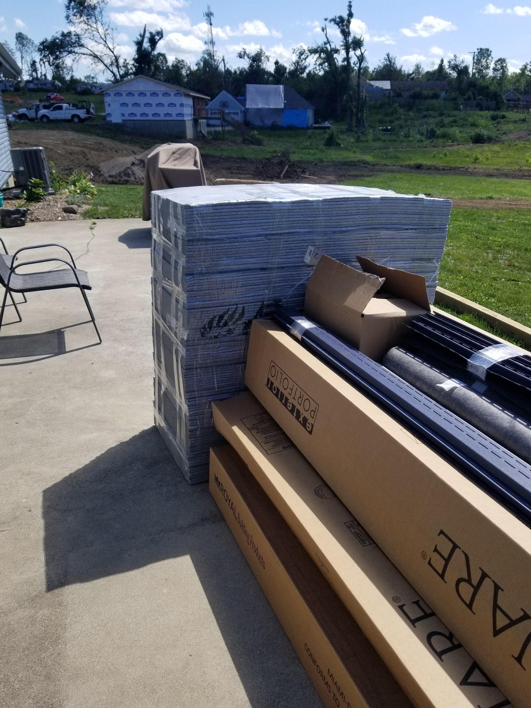 Boxes of siding and metal stacked by the house, storm-damaged trees beyond, Beavercreek, Ohio.