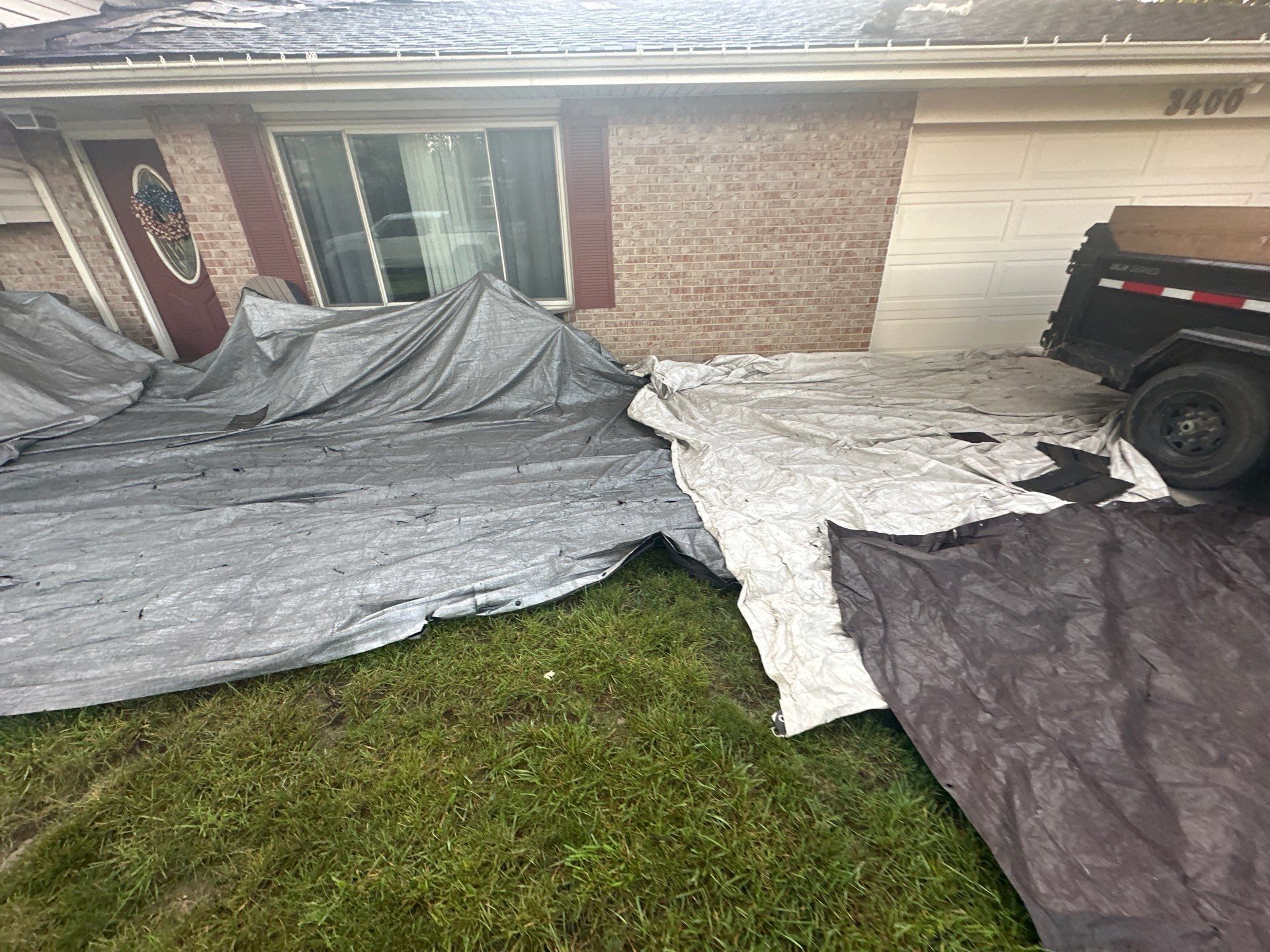 Tarps covering the front walk and lawn in front of the brick ranch, with the dumpster trailer by the drive, Dayton, Ohio.