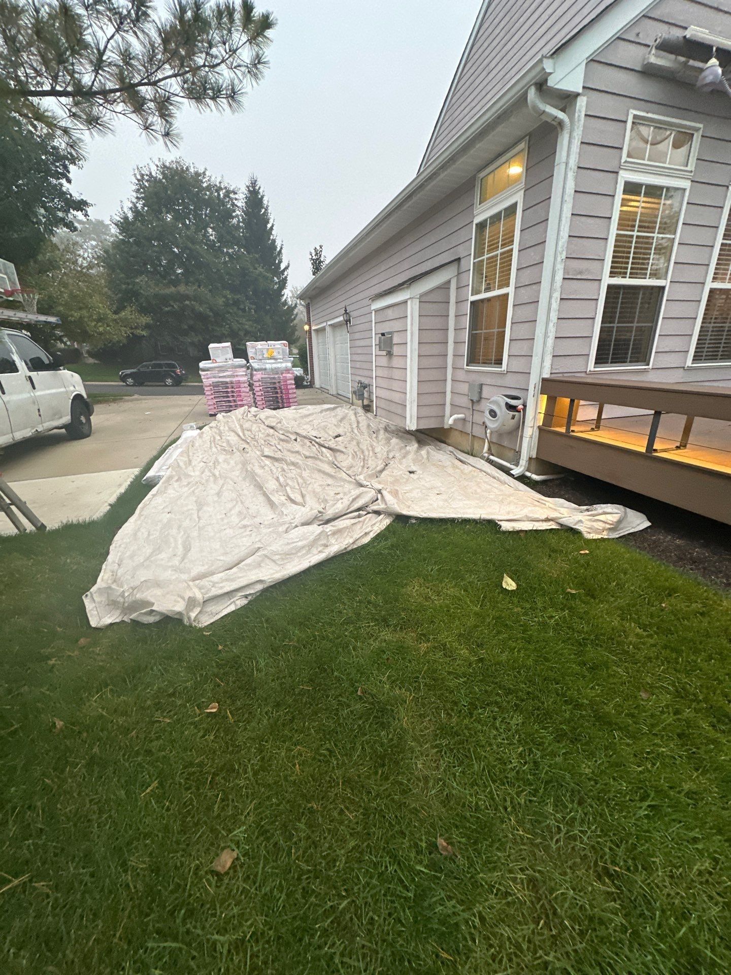 A tarp spread over the lawn beside the driveway, with shingle pallets by the garage, Beavercreek, Ohio.