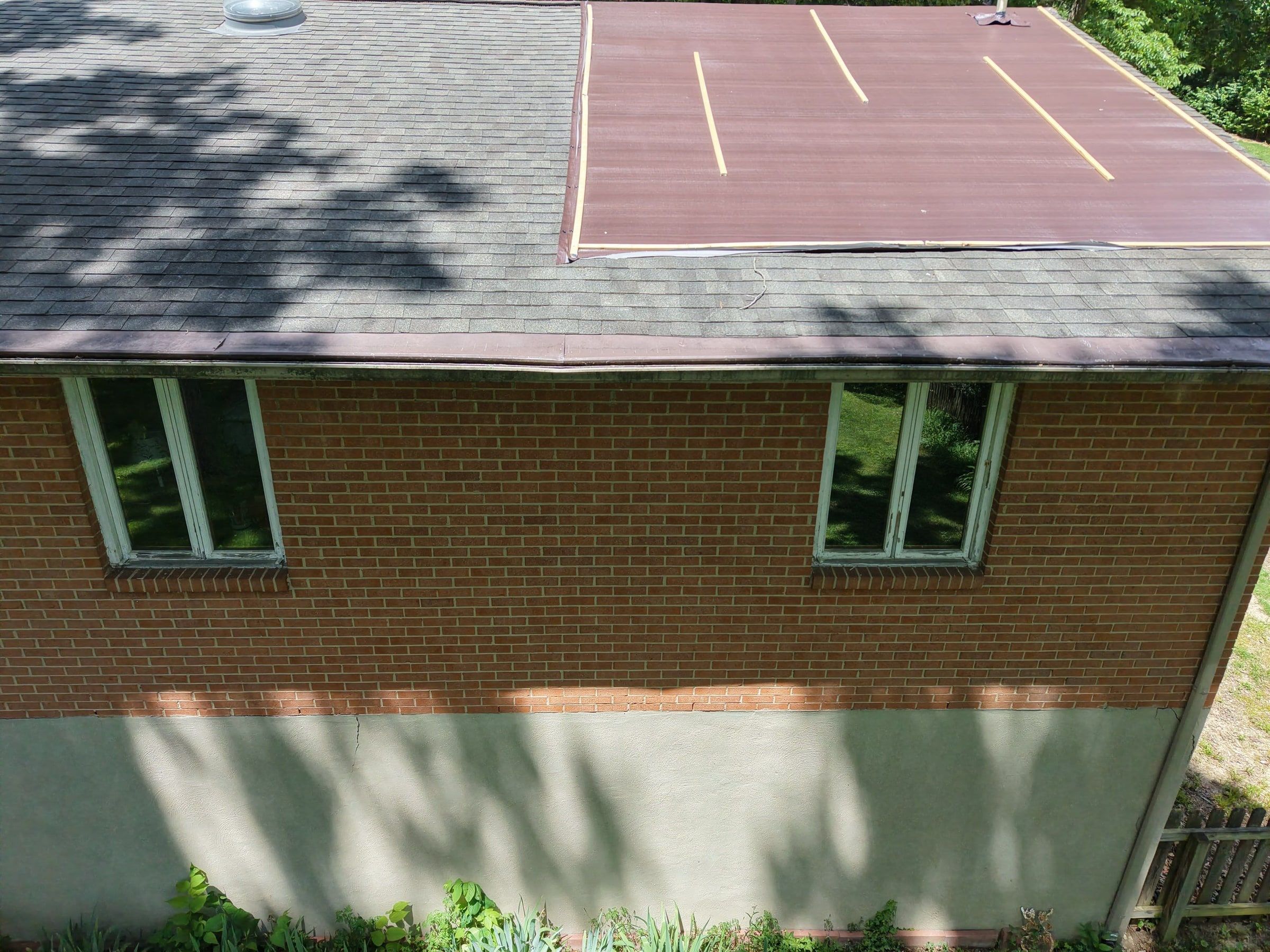 An older shingle roof with a brown tarp held down by boards over the tree damage.